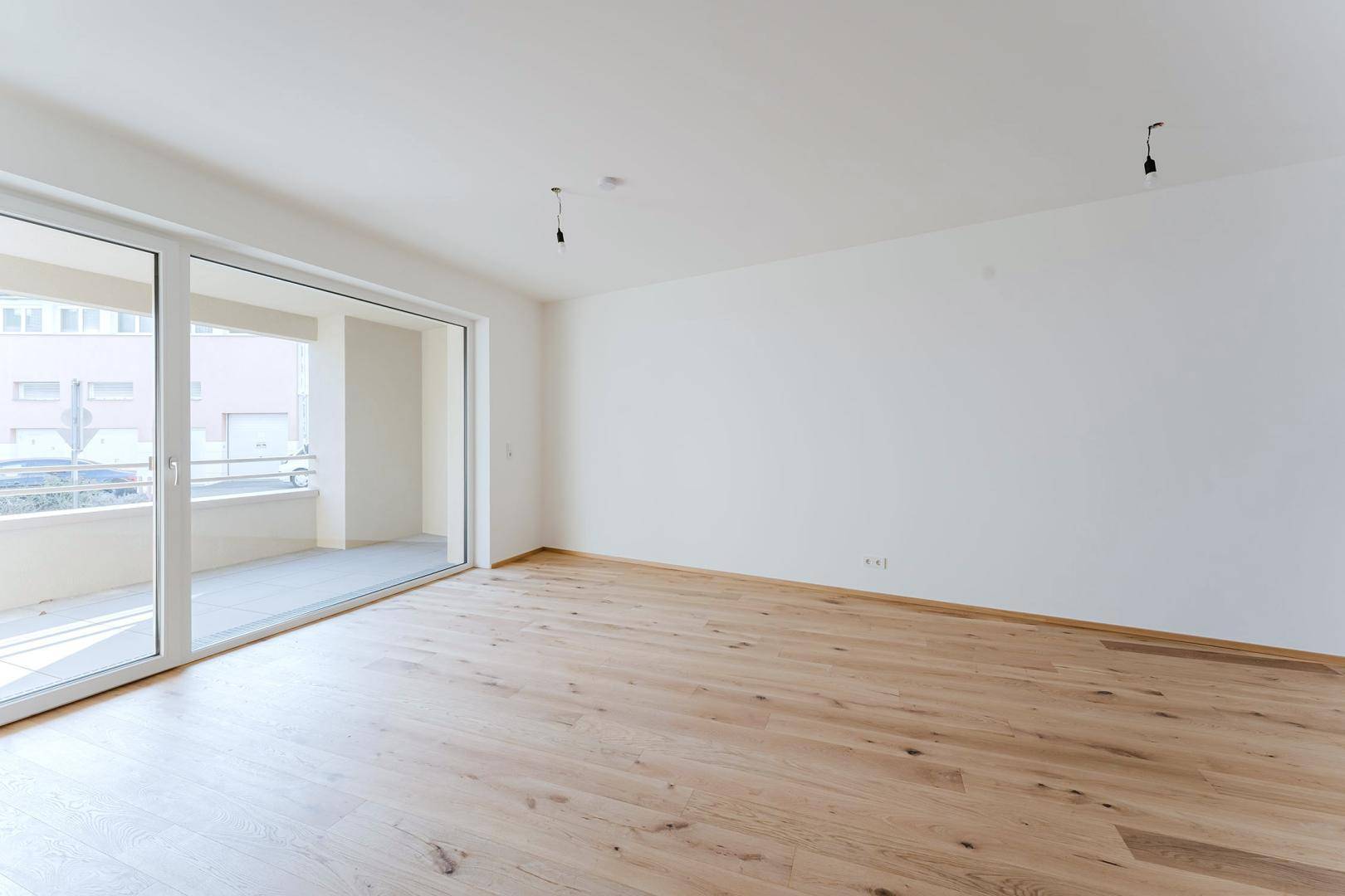 Helles, unmöbliertes Zimmer mit Holzfußboden und direktem Zugang zu einem sonnigen Balkon.