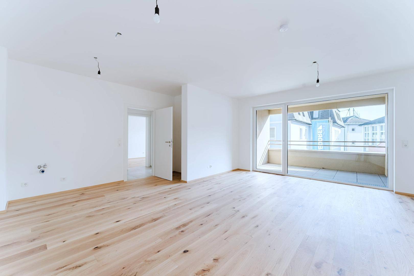 Helles, unmöbliertes Zimmer mit Holzparkett und direktem Zugang zu einem sonnigen Balkon.