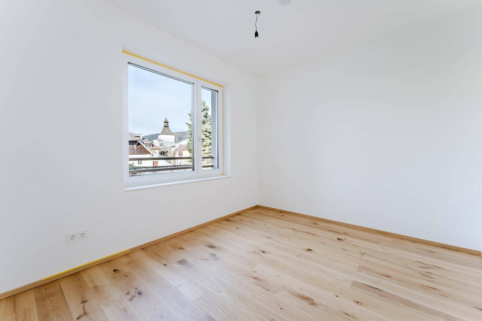 Helles Zimmer mit Holzfußboden und Fenster, das einen Blick auf die Umgebung ermöglicht.