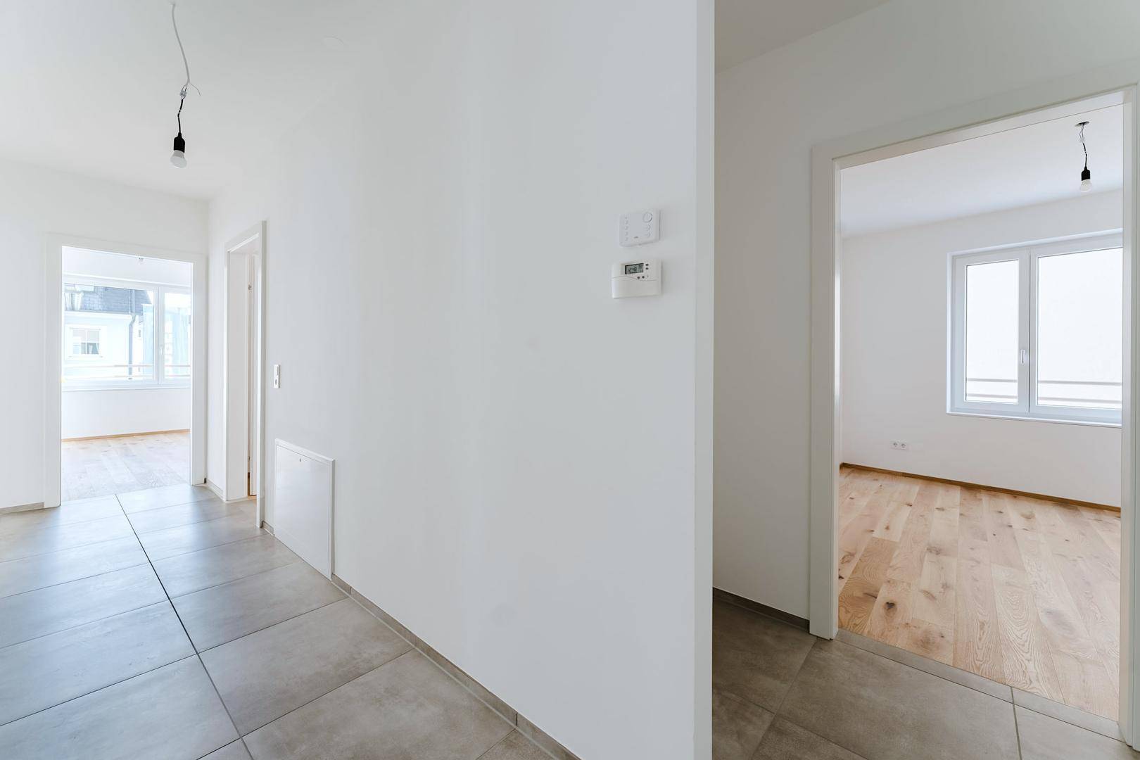 Heller Flur mit modernen grauen Fliesen und Zugang zu weiteren Zimmern mit Holzfußboden.