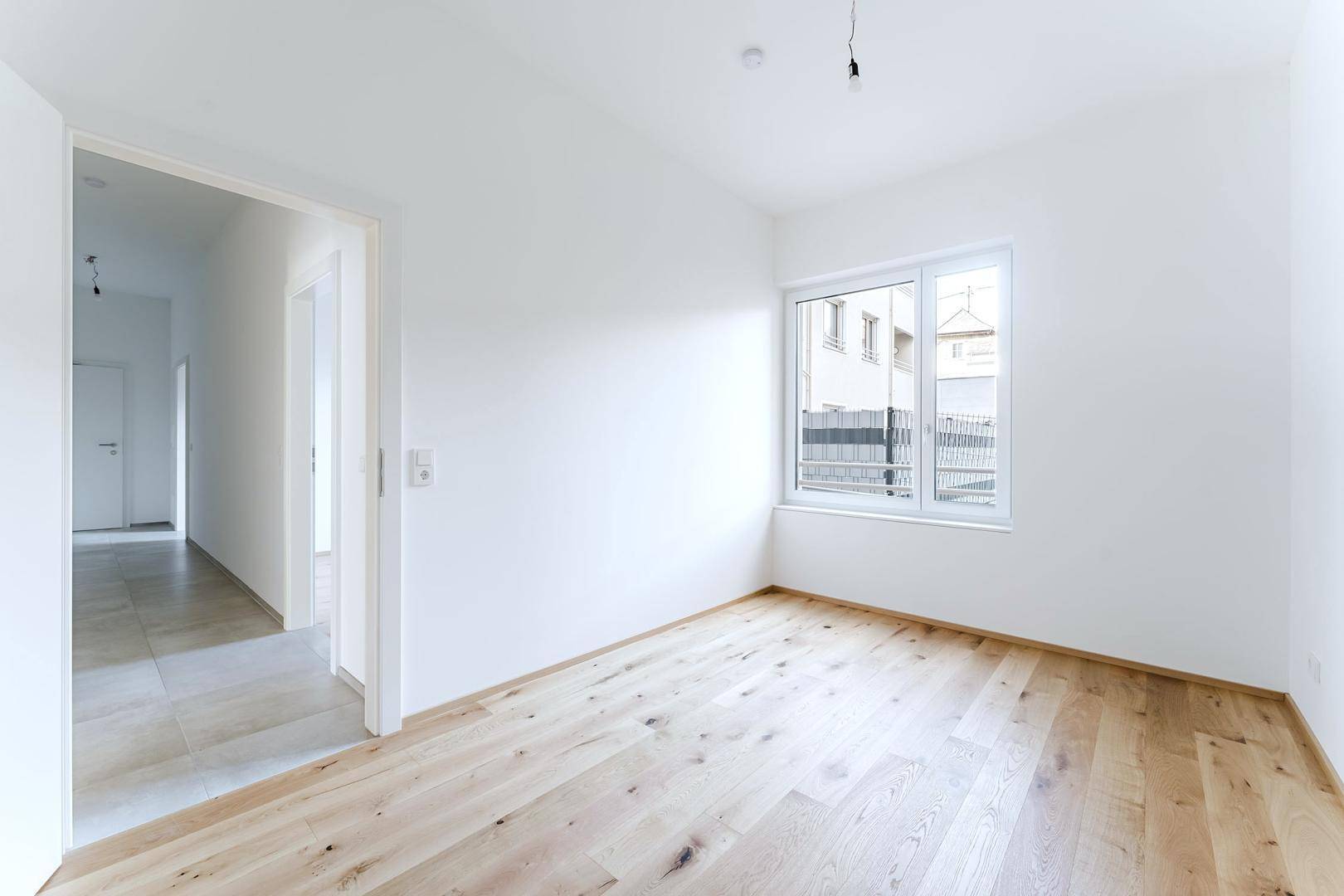 Leeres Zimmer mit hellem Holzfußboden und Fenster, das viel Tageslicht hereinlässt.