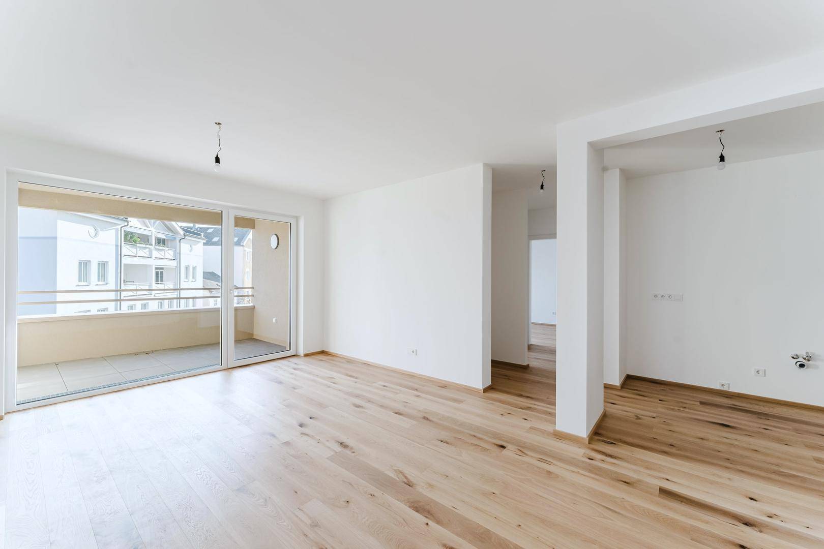 Heller, leerer Wohnbereich mit Holzboden und großzügigem Zugang zu einem Balkon.