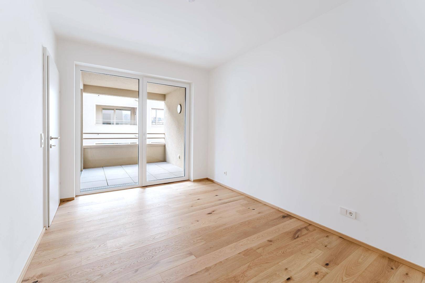 Helles, unmöbliertes Zimmer mit Holzboden und direktem Zugang zu einem Balkon.