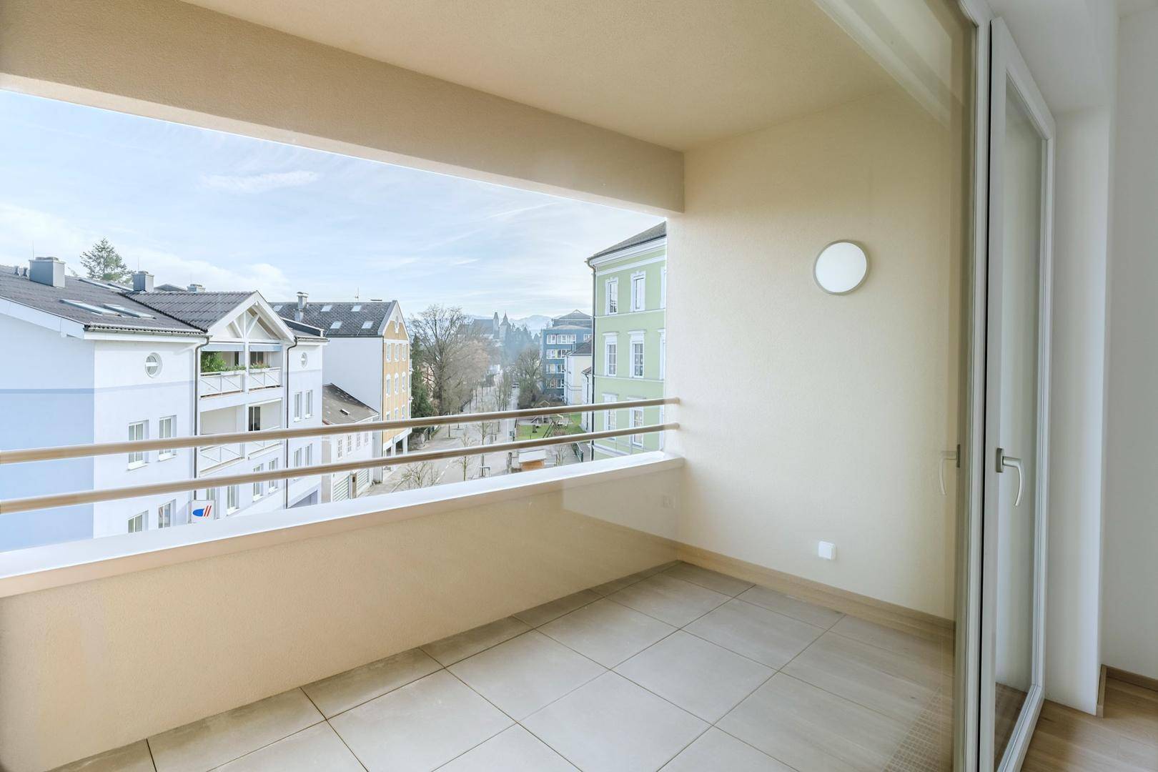 Geräumiger Balkon mit Fliesenboden und Blick auf die umliegenden Gebäude und die Straße.