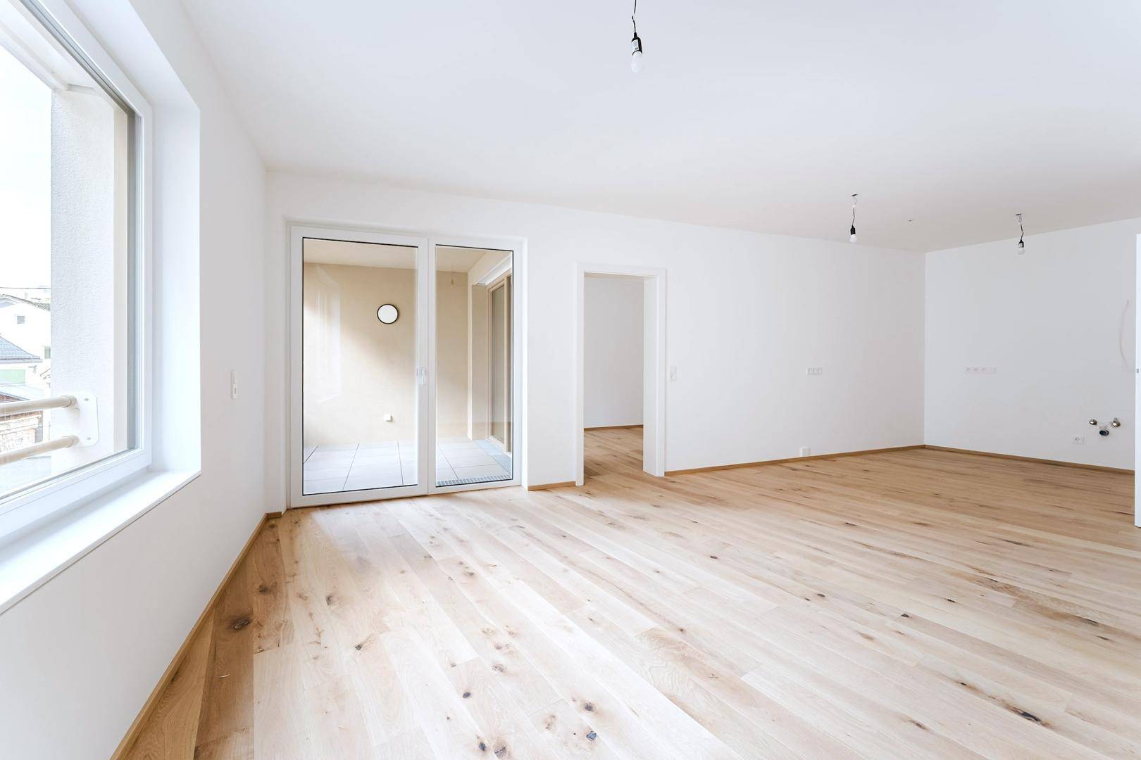 Heller, leerer Raum mit großen Fenstern und Holzboden, bereit zum Einzug.