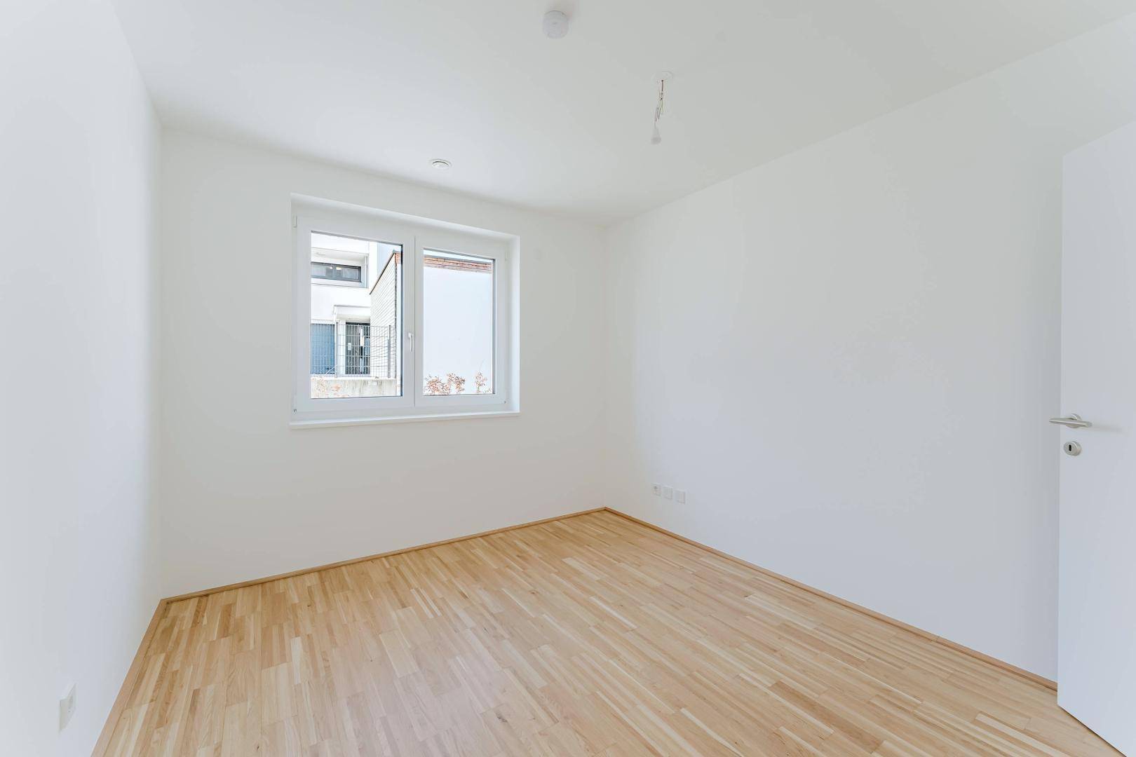 Helles Schlafzimmer mit Holzboden und einem Fenster, das den Blick auf die Umgebung freigibt.