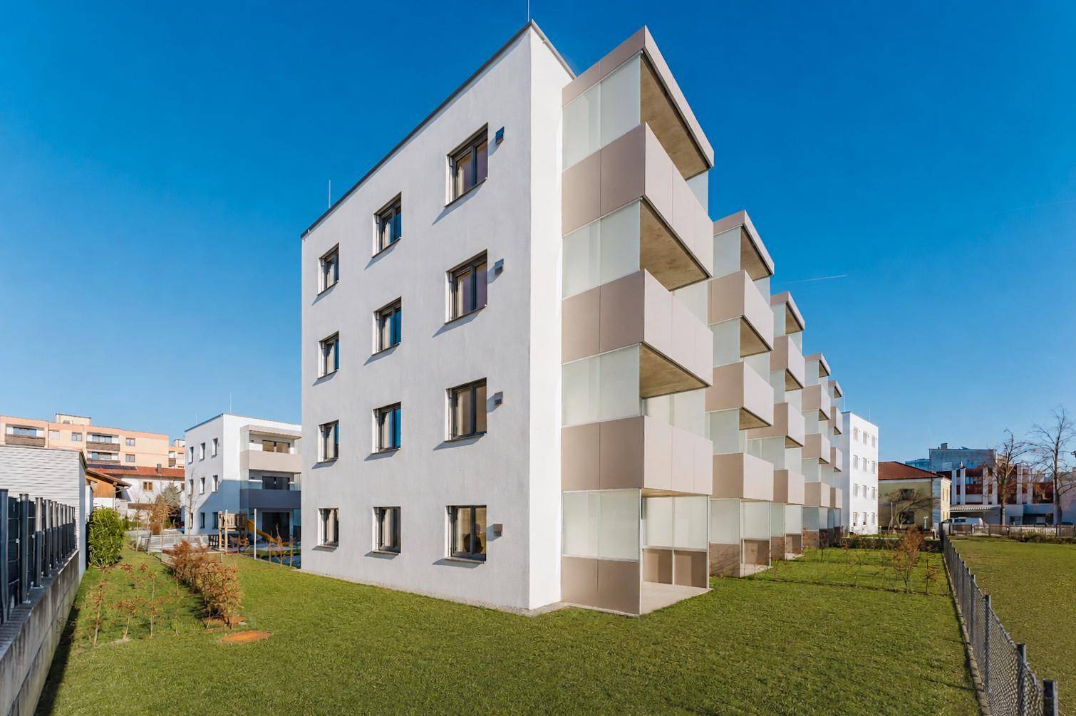 Moderne Wohnanlage mit weißer Fassade, Balkonen und gepflegten Grünflächen unter blauem Himmel.