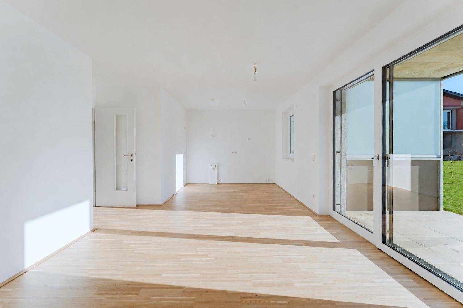 Geräumiger, heller Raum mit Holzboden und Zugang zur Terrasse, ideal für offenes Wohnen.