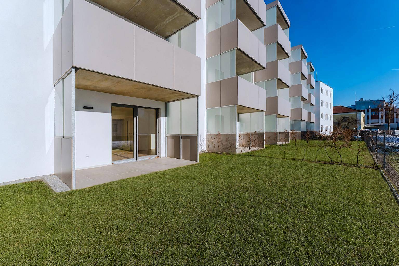 Erdgeschoss-Terrasse mit direktem Zugang zum Gartenbereich und Blick auf die moderne Wohnanlage.