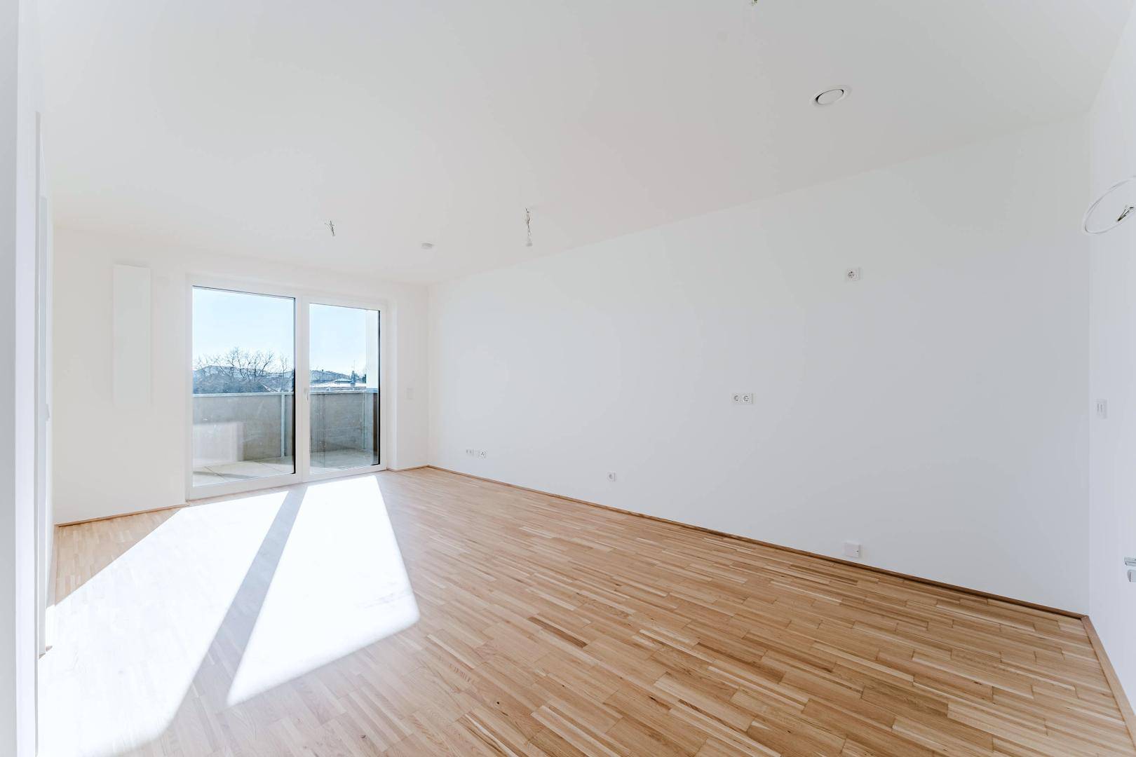 Geräumiges, helles Zimmer mit Parkettboden und Zugang zu einem Balkon.