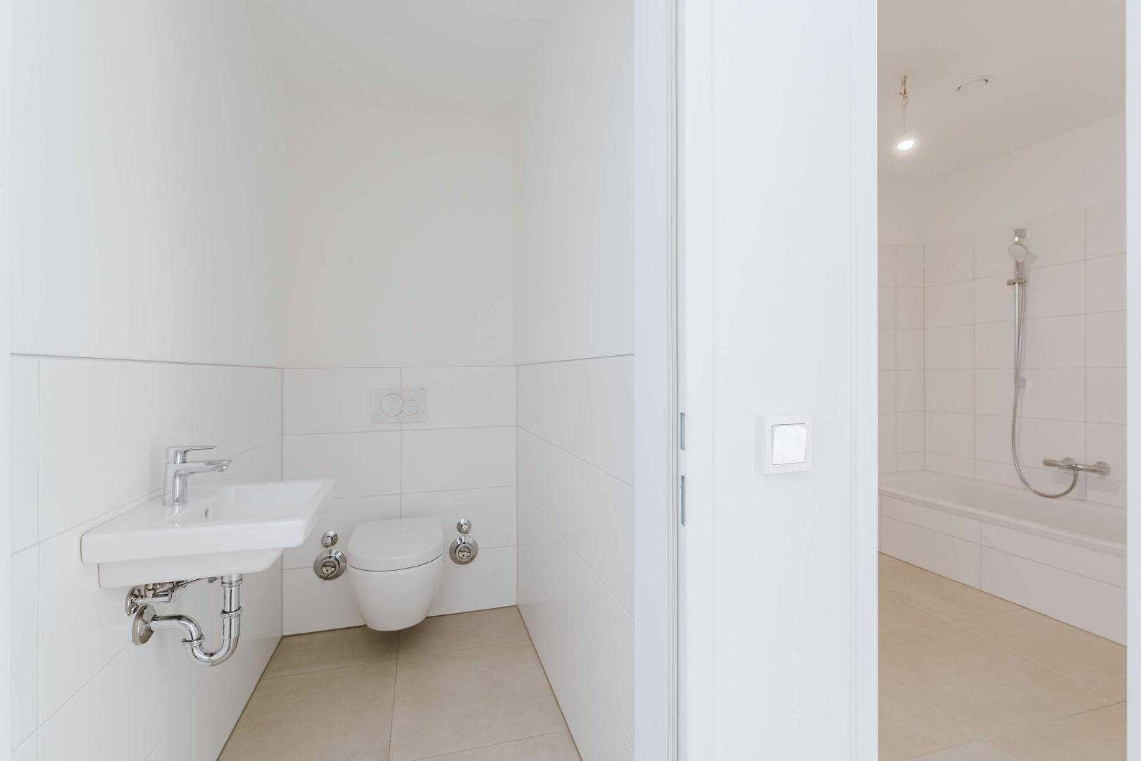 Separates WC mit wandhängender Toilette und Waschbecken, angrenzend an das Badezimmer.