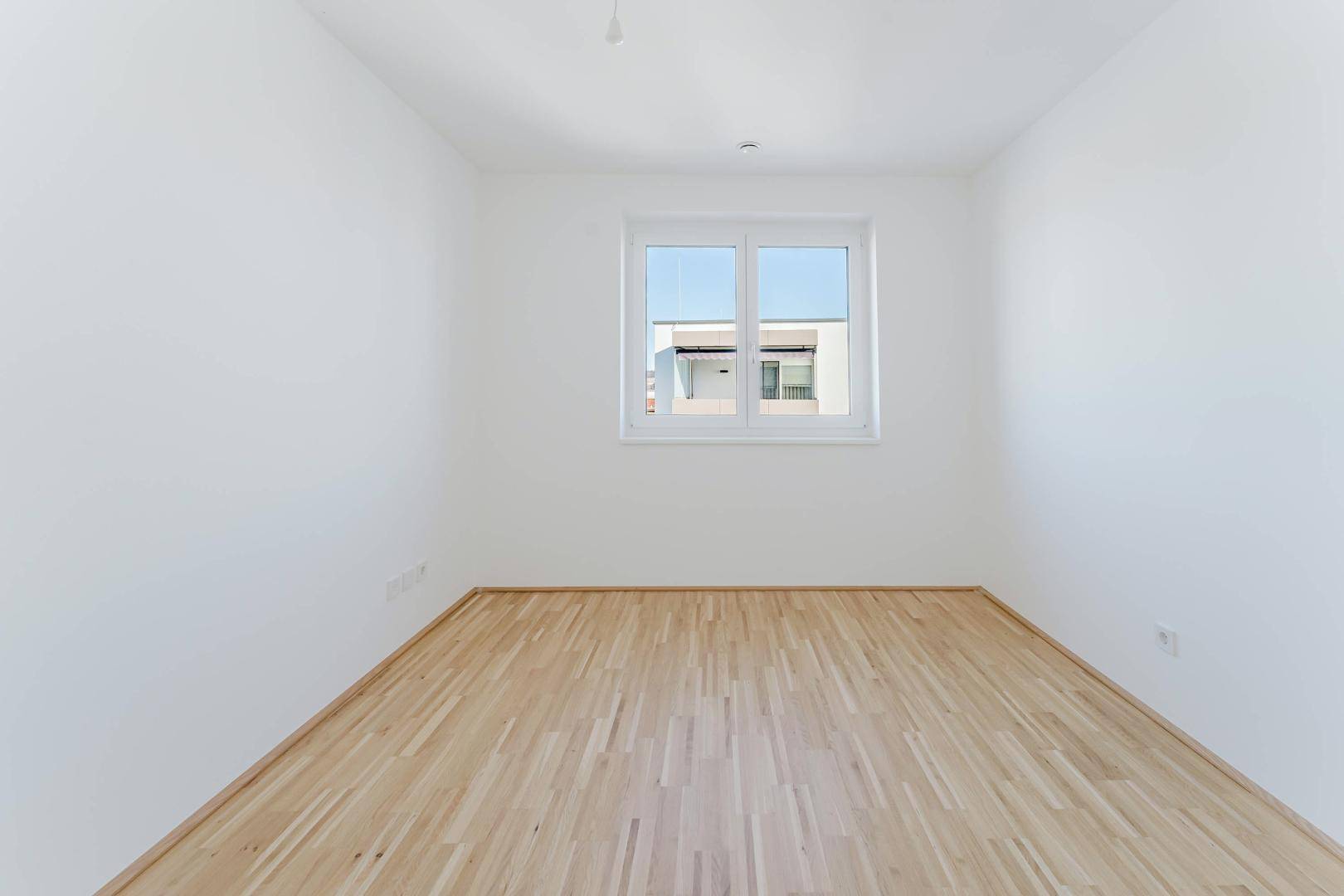 Freundliches Zimmer mit Parkettboden und weitem Blick durch das große Fenster.