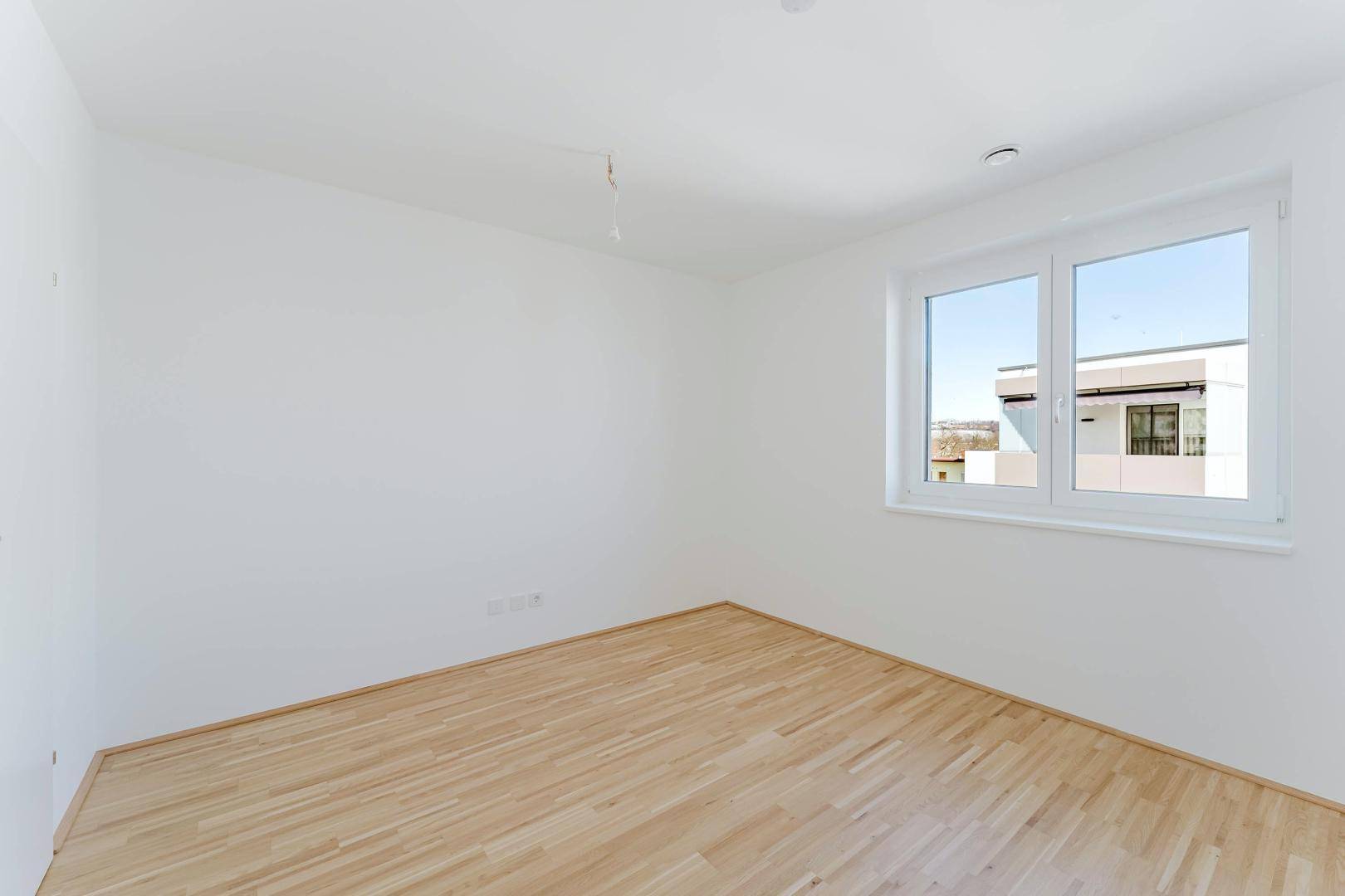Helles Schlafzimmer mit Parkettboden und großem Fenster, bereit zur individuellen Gestaltung.