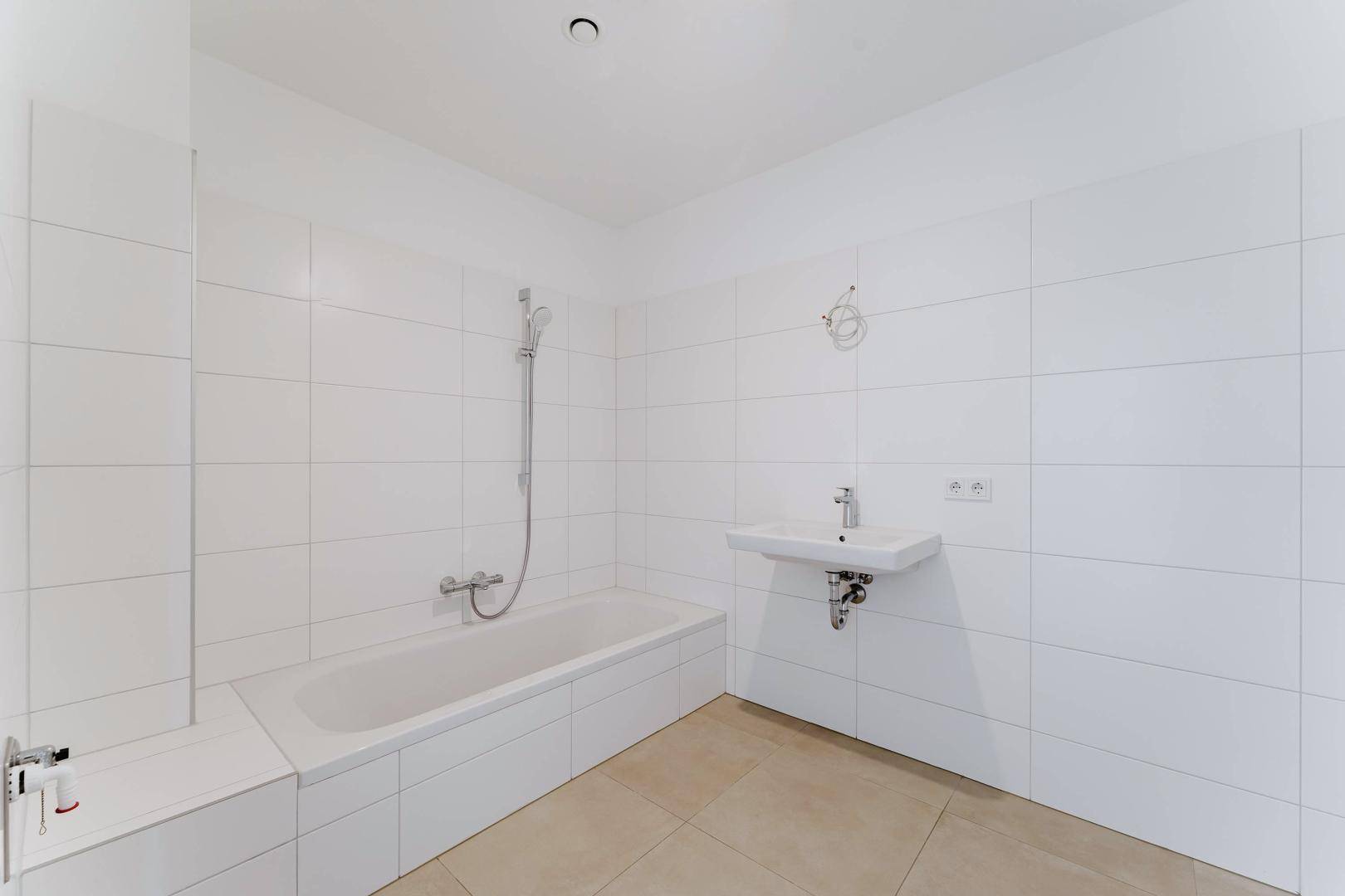 Modernes Badezimmer mit Badewanne, Duschvorrichtung und hellem Fliesenboden.