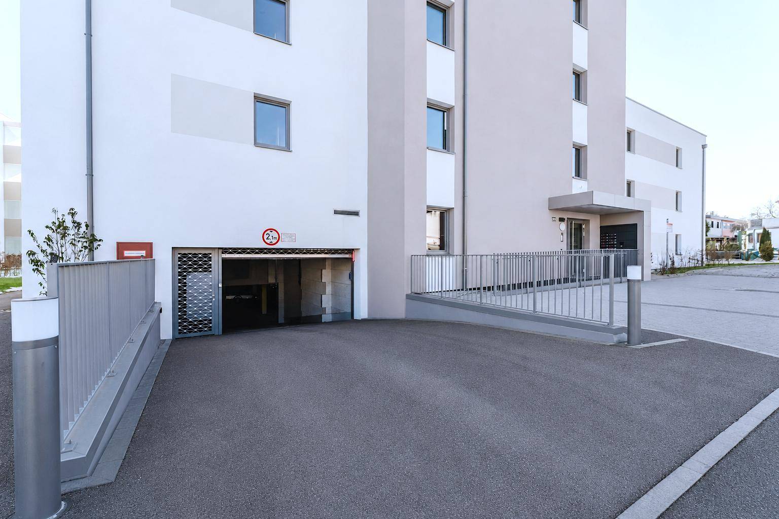 Zufahrt zur Tiefgarage einer modernen Wohnanlage mit Rampe und Sicherheitstor.