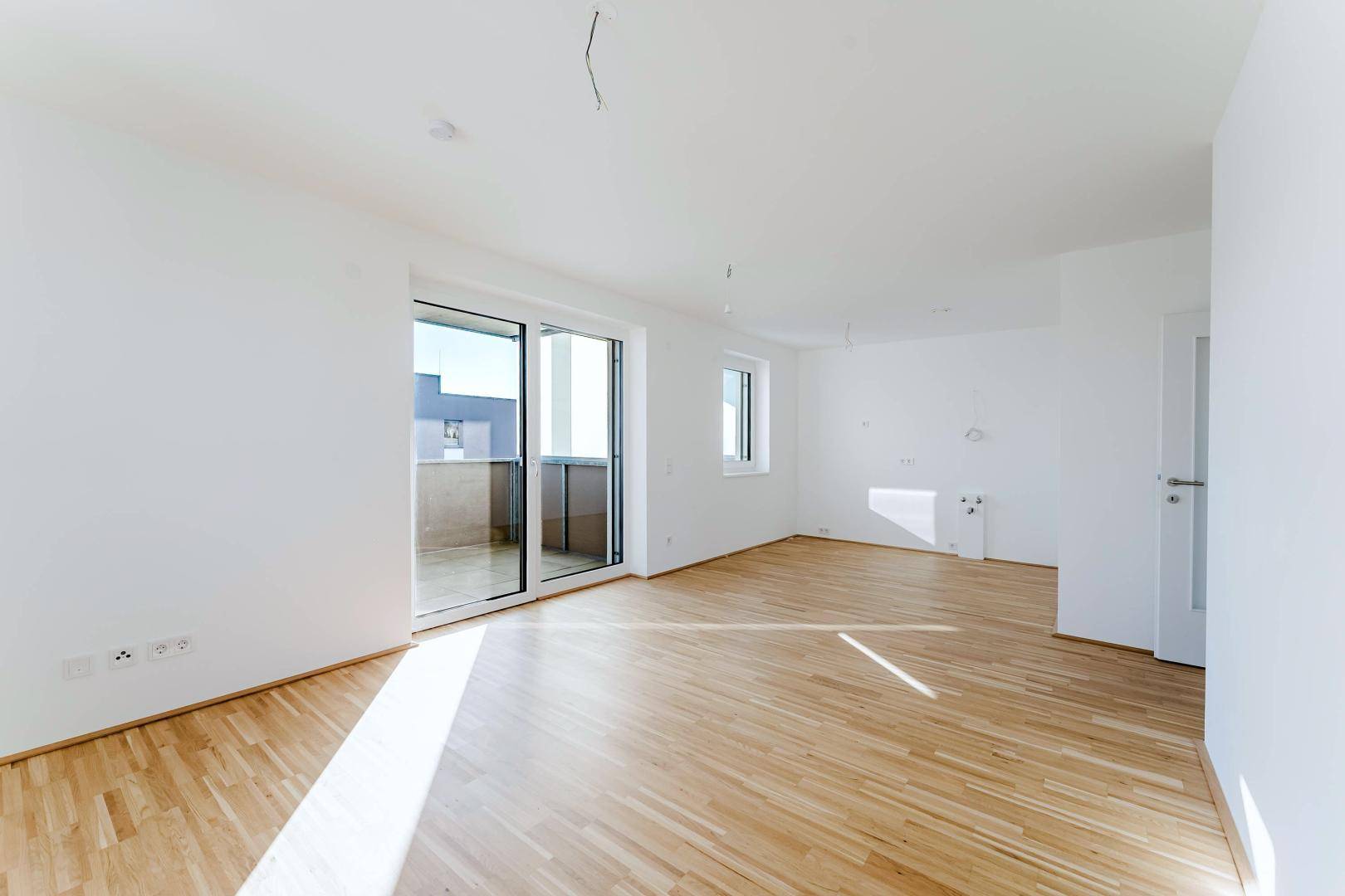 Geräumiger, heller Wohnraum mit Parkettboden und Schiebetür zum Außenbereich.