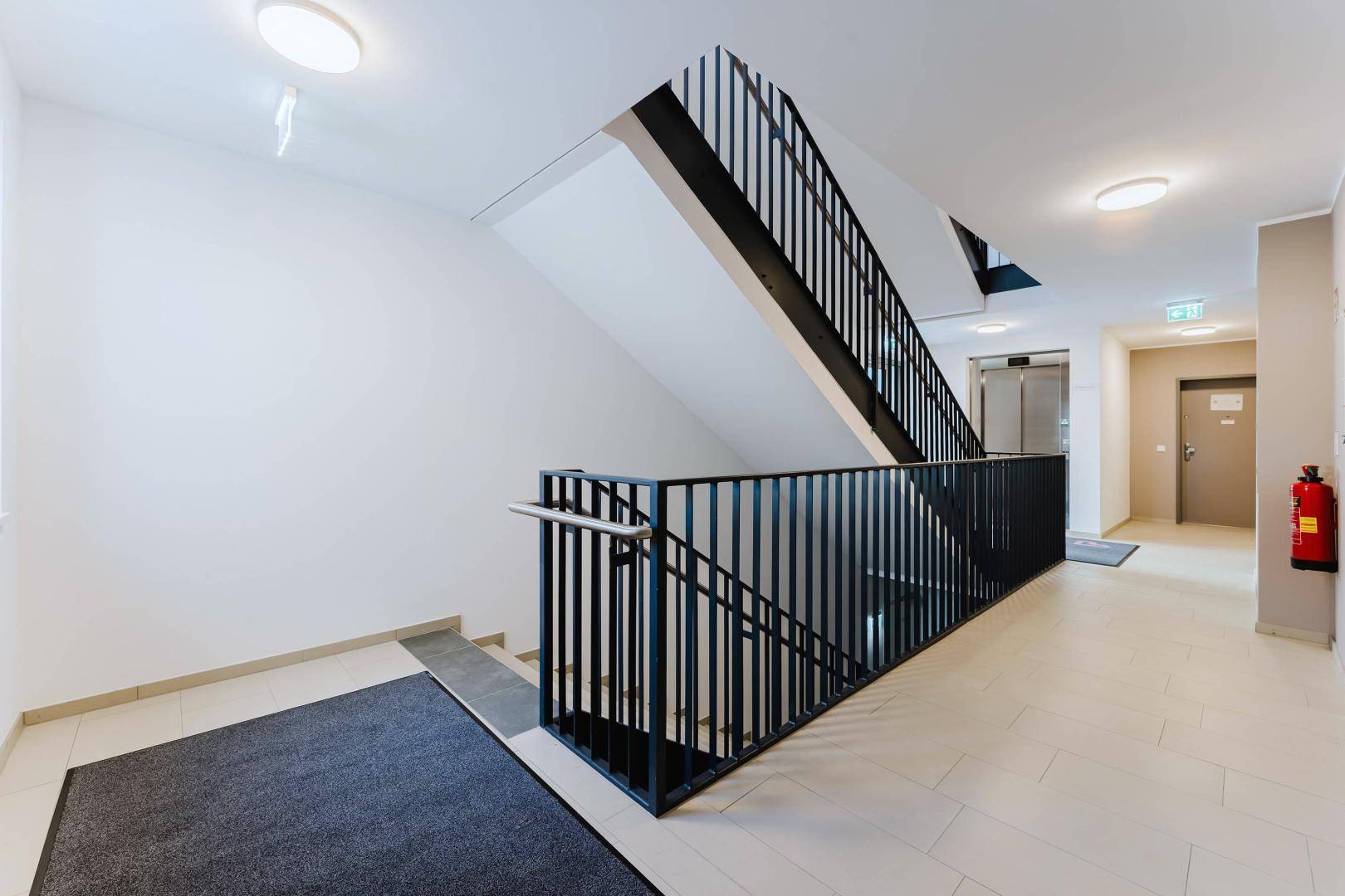 Geräumiges Treppenhaus mit modernem Design und sichtbarem Aufzug im Hintergrund.