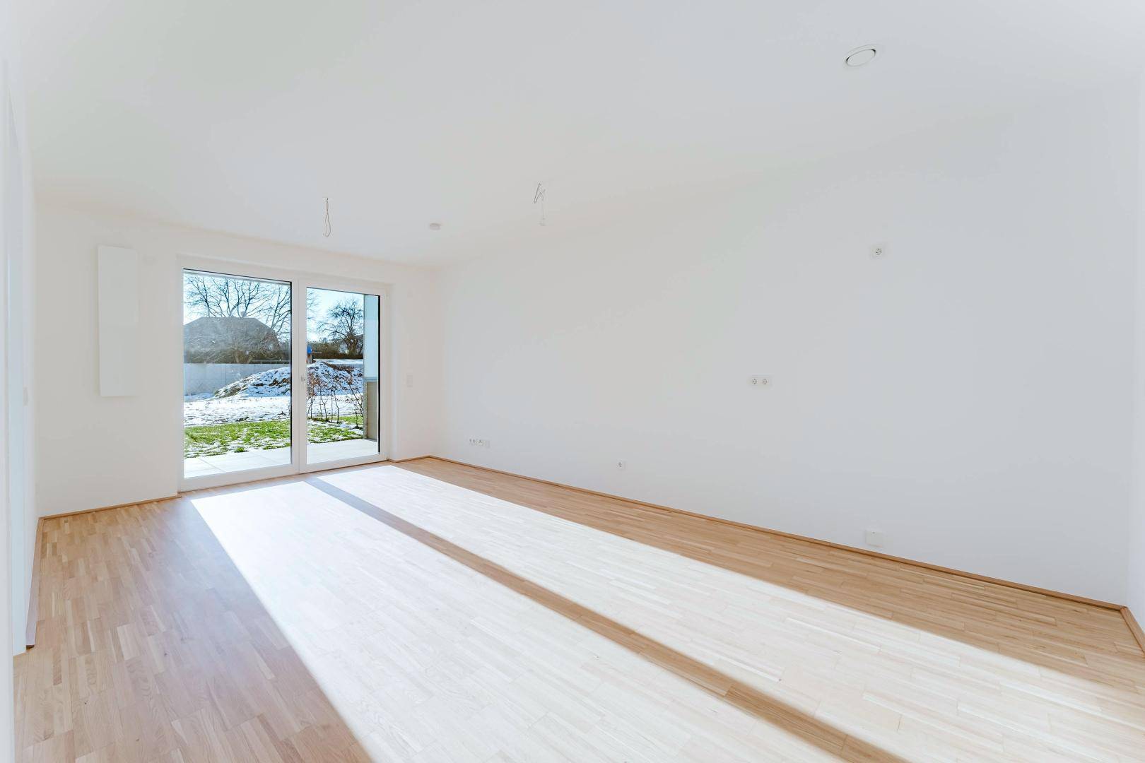 Heller, leerer Raum mit großen Schiebetüren und Blick ins Grüne, ideal für ein Wohnzimmer.