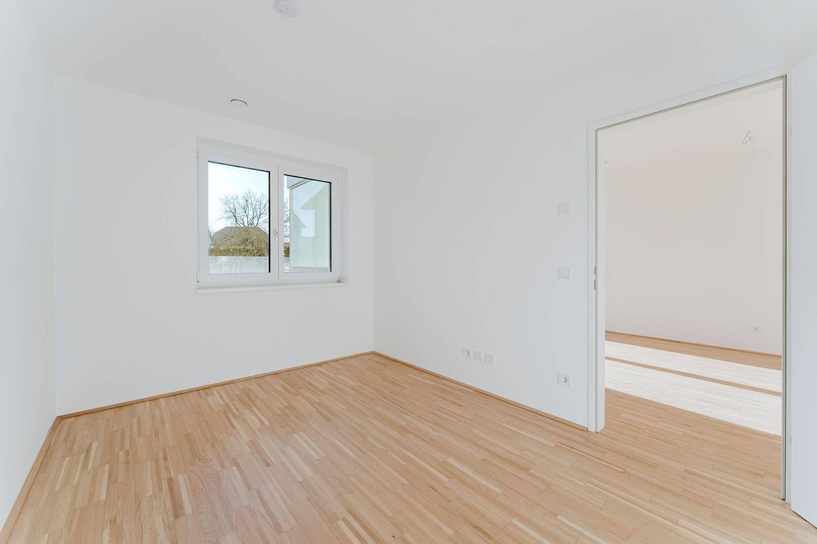 Leeres Schlafzimmer mit hellem Holzboden und Fenster, bereit zur individuellen Gestaltung.