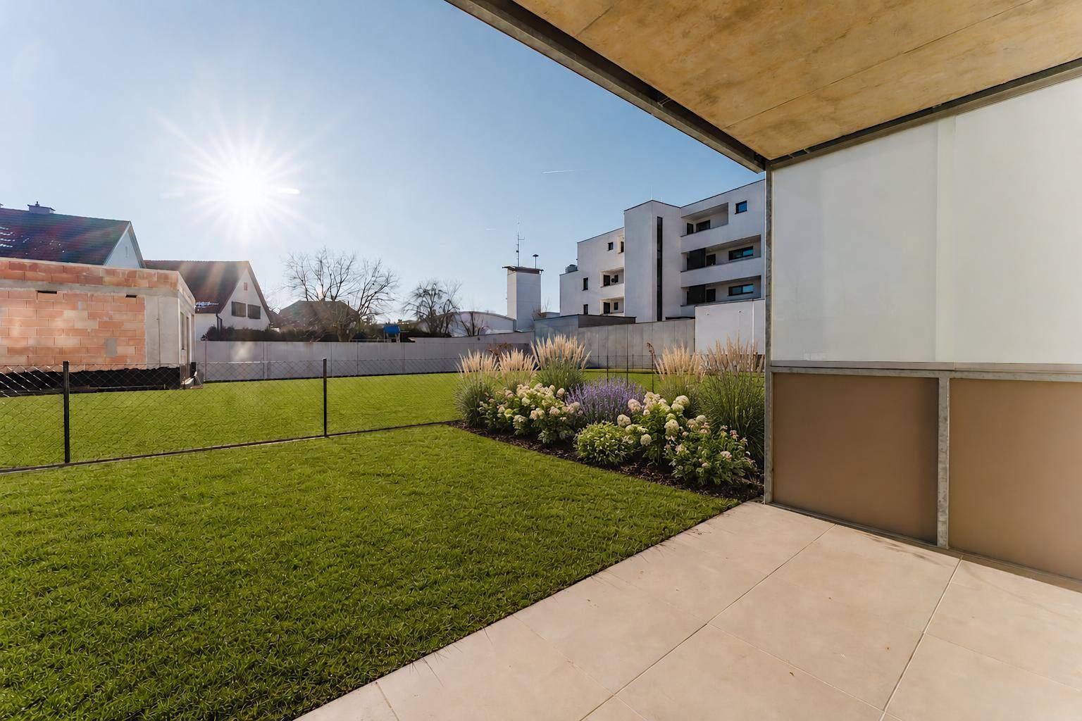 Sonniger Terrassenbereich mit Rasenfläche und Blumenbeeten, ideal zum Entspannen im Freien.