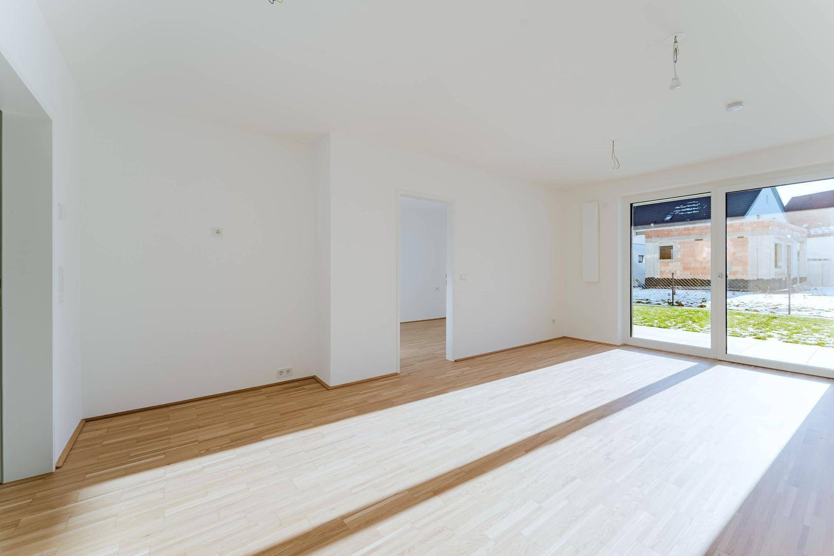 Geräumiger, heller Wohnbereich mit Holzboden und offener Verbindung zu weiteren Zimmern.