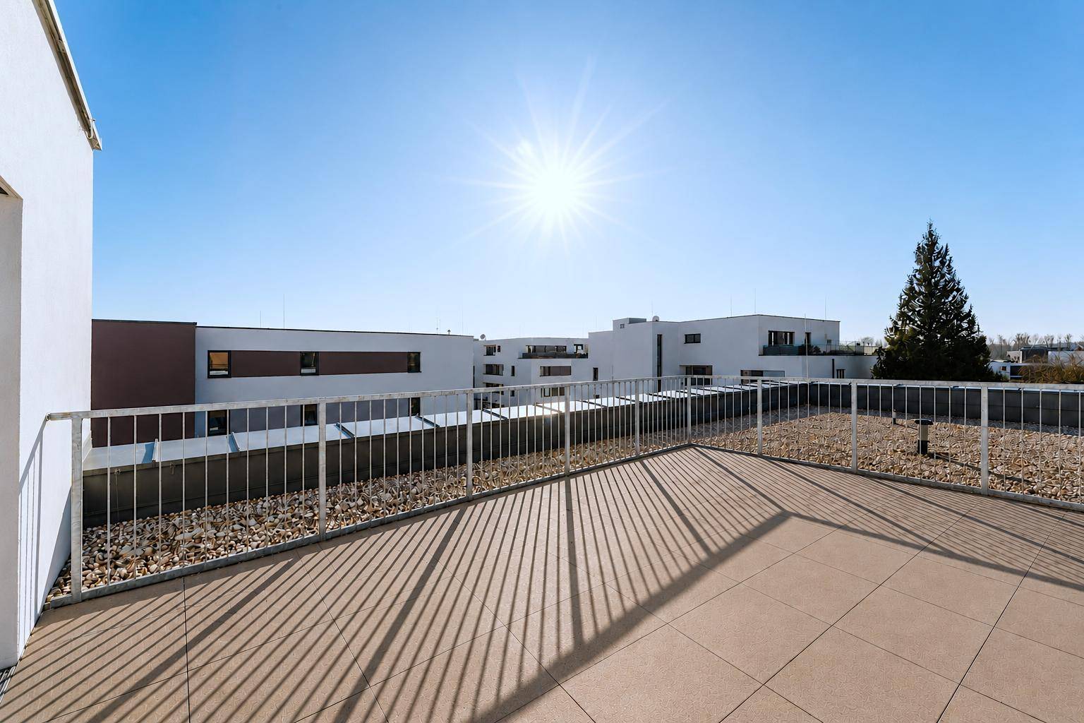 Große, sonnige Dachterrasse mit Fliesenboden und Blick auf die umliegenden Gebäude.