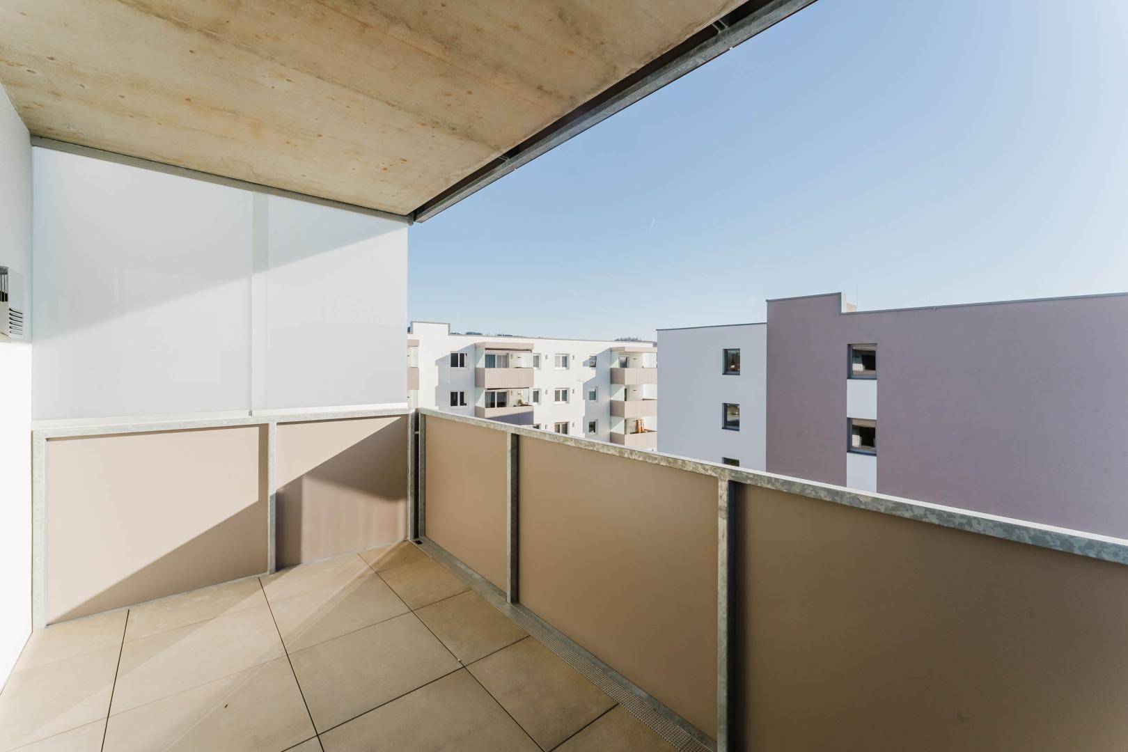 Kleiner Balkon mit Fliesenboden und Blick auf die modernen Wohngebäude.