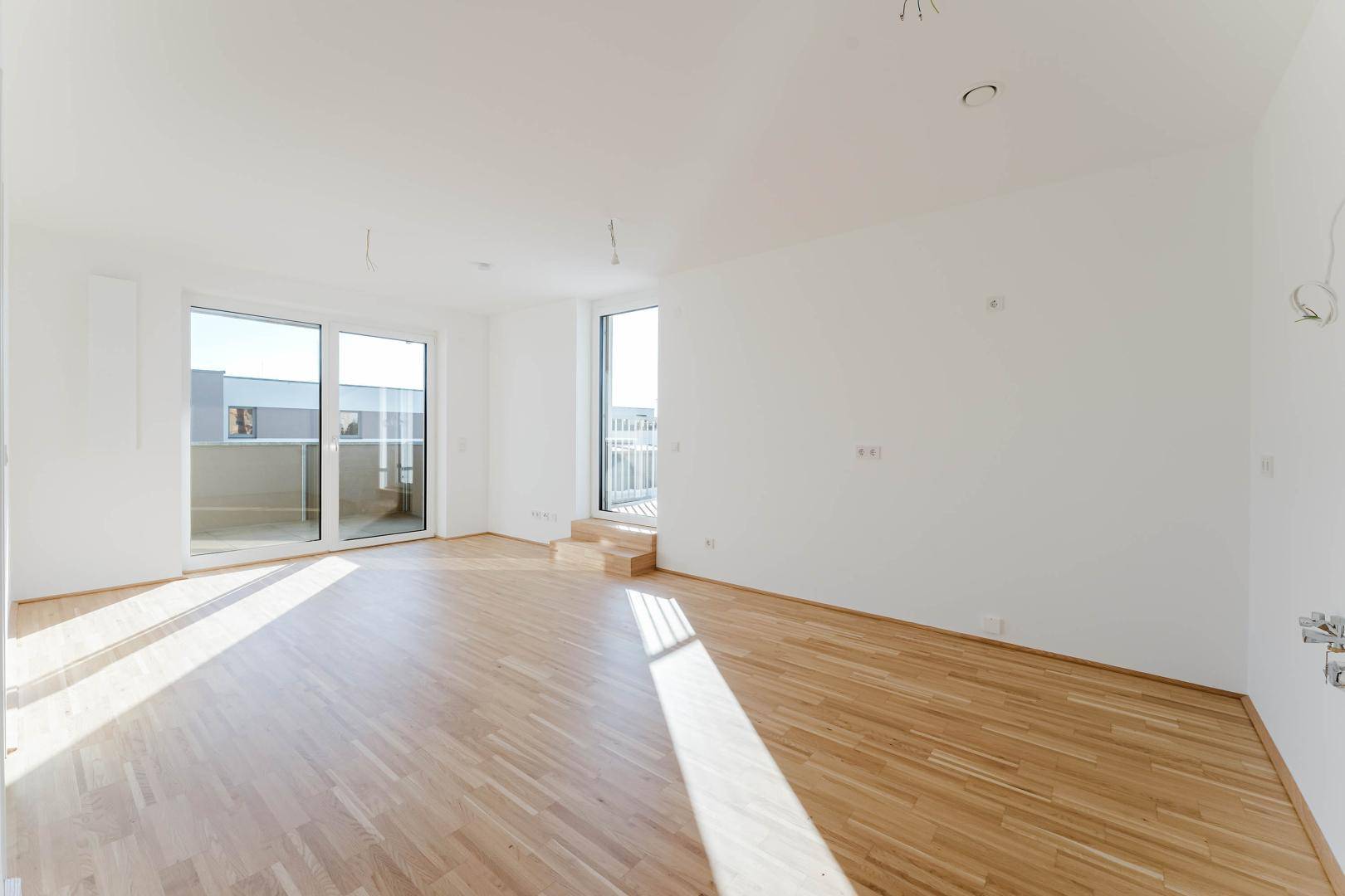Geräumiges, helles Zimmer mit Holzboden und großen Schiebetüren zu einem Außenbereich.