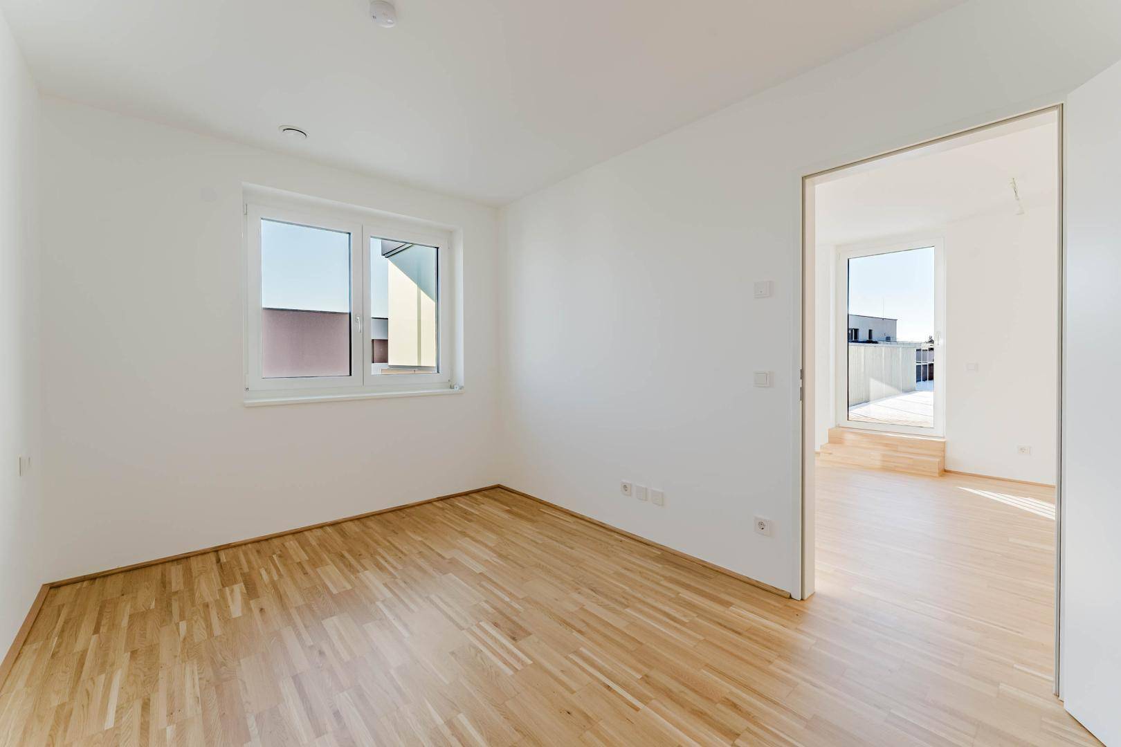 Unmöbliertes Zimmer mit Parkettboden und einem Fenster, das viel Tageslicht hereinlässt.