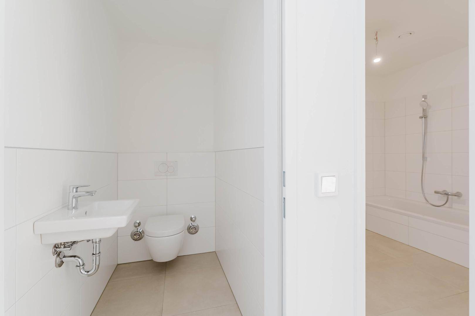 Separates Gäste-WC mit Wand-WC und kleinem Waschbecken, angrenzend an ein Badezimmer.