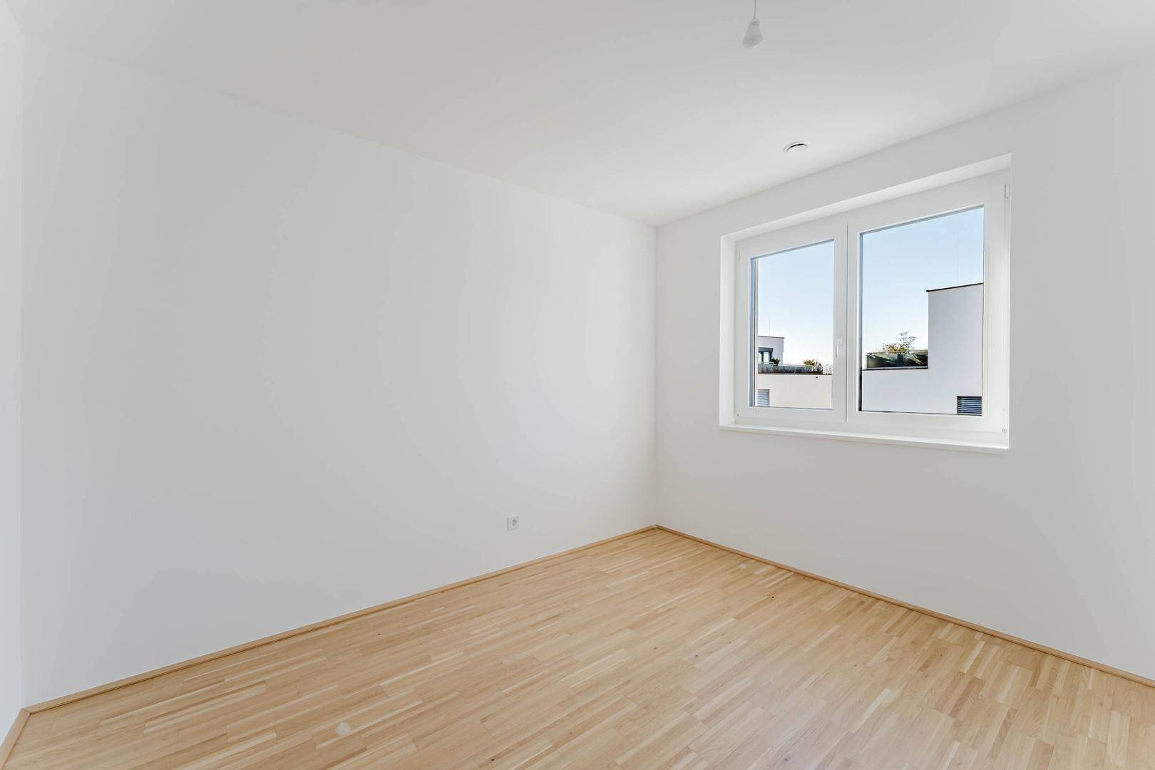 Unmöbliertes Zimmer mit hellem Parkettboden und Fenster, ideal als Schlaf- oder Arbeitszimmer.