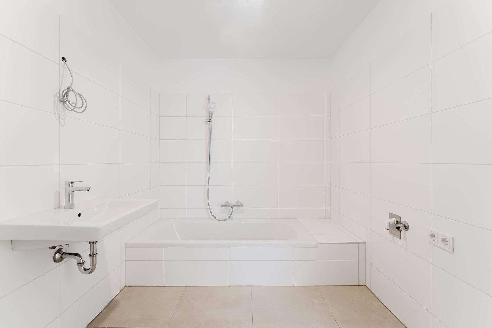 Sauberes Badezimmer mit weißen Wandfliesen, Badewanne und modernem Waschbecken.