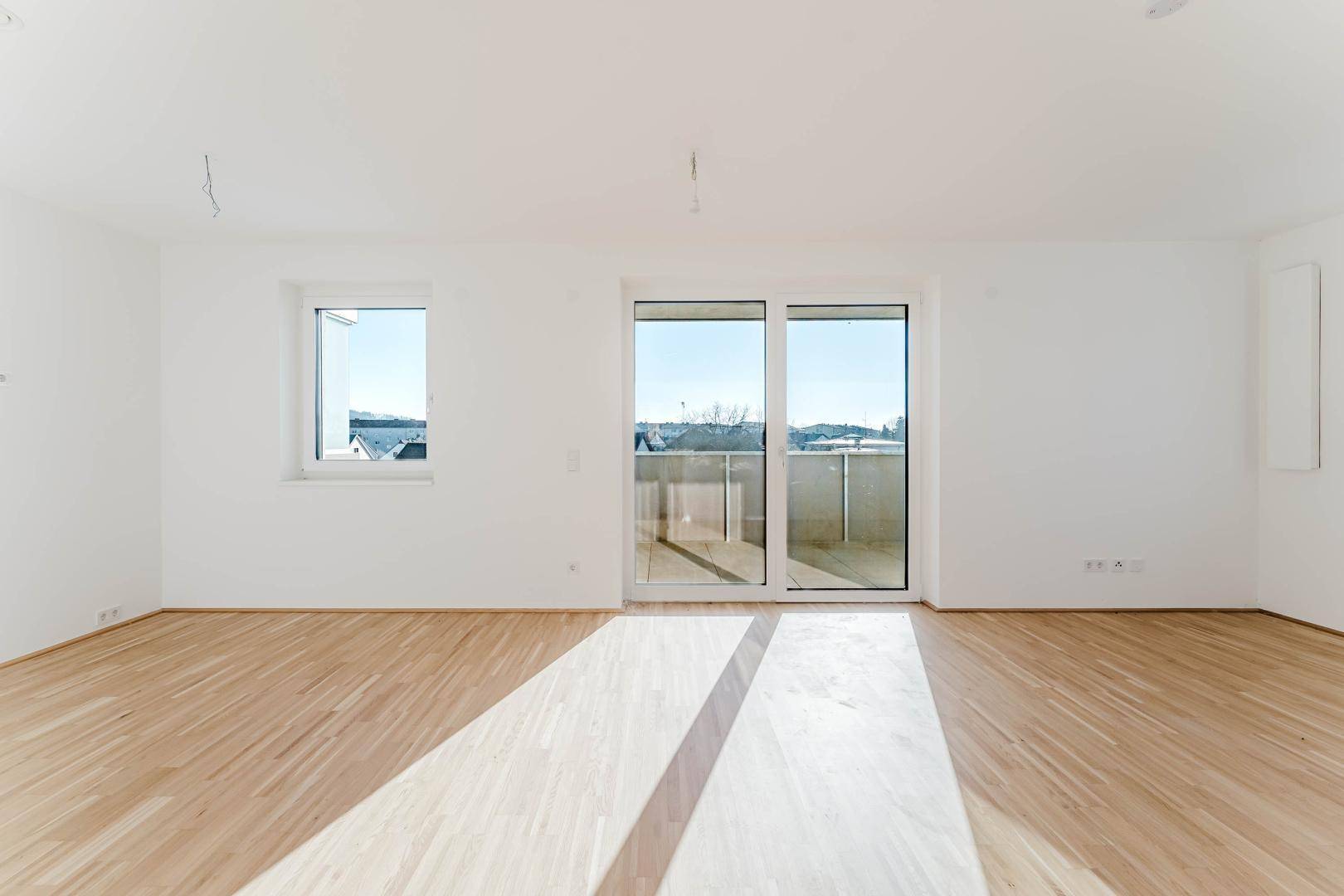 Geräumiger, heller Wohnbereich mit Parkettboden und Balkonzugang in einem Neubau.