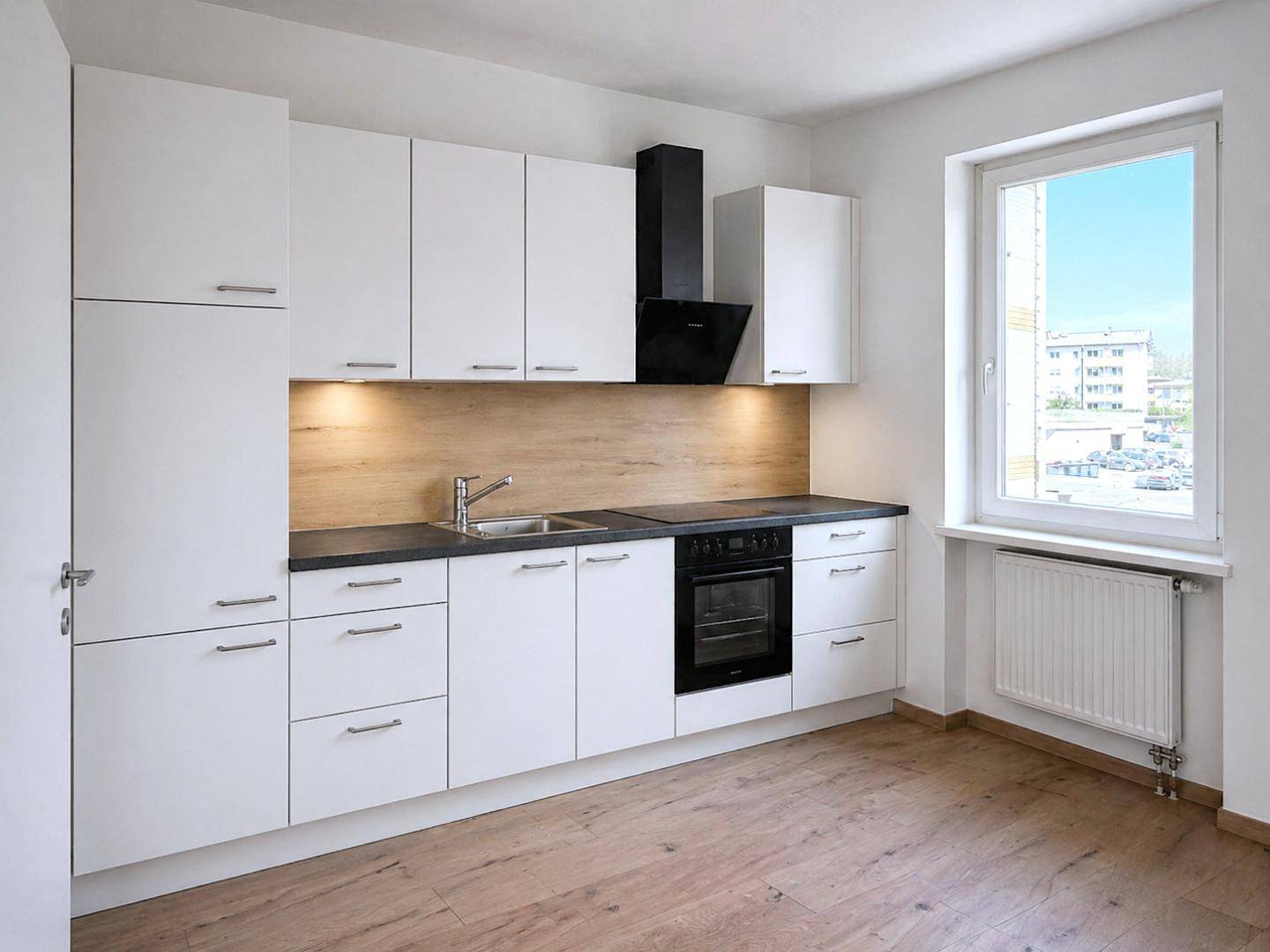Moderne Einbauküche mit weißen Schränken, dunkler Arbeitsplatte und Fenster.