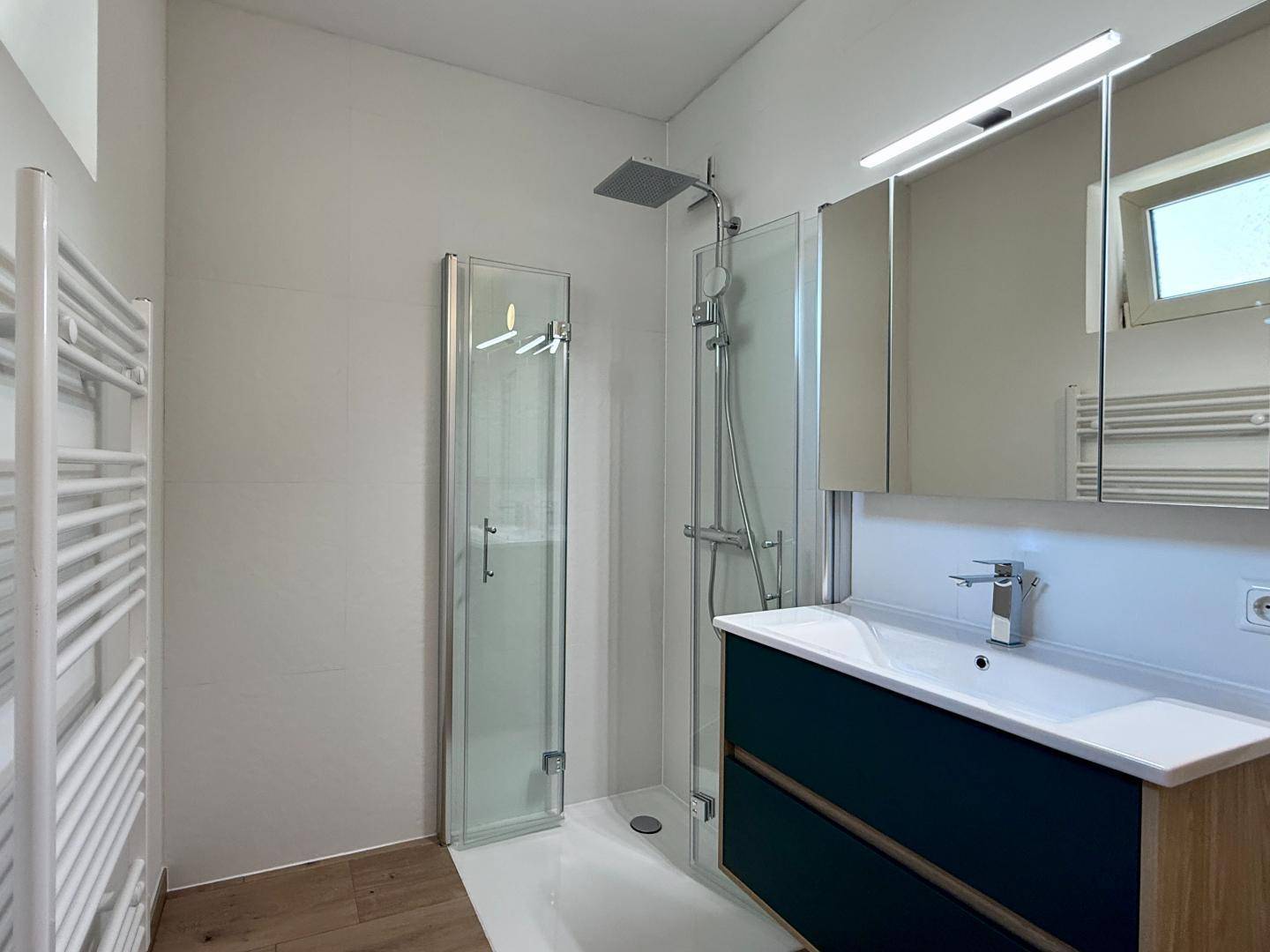Helles Badezimmer mit moderner Duschkabine, Waschbecken und beheiztem Handtuchhalter.
