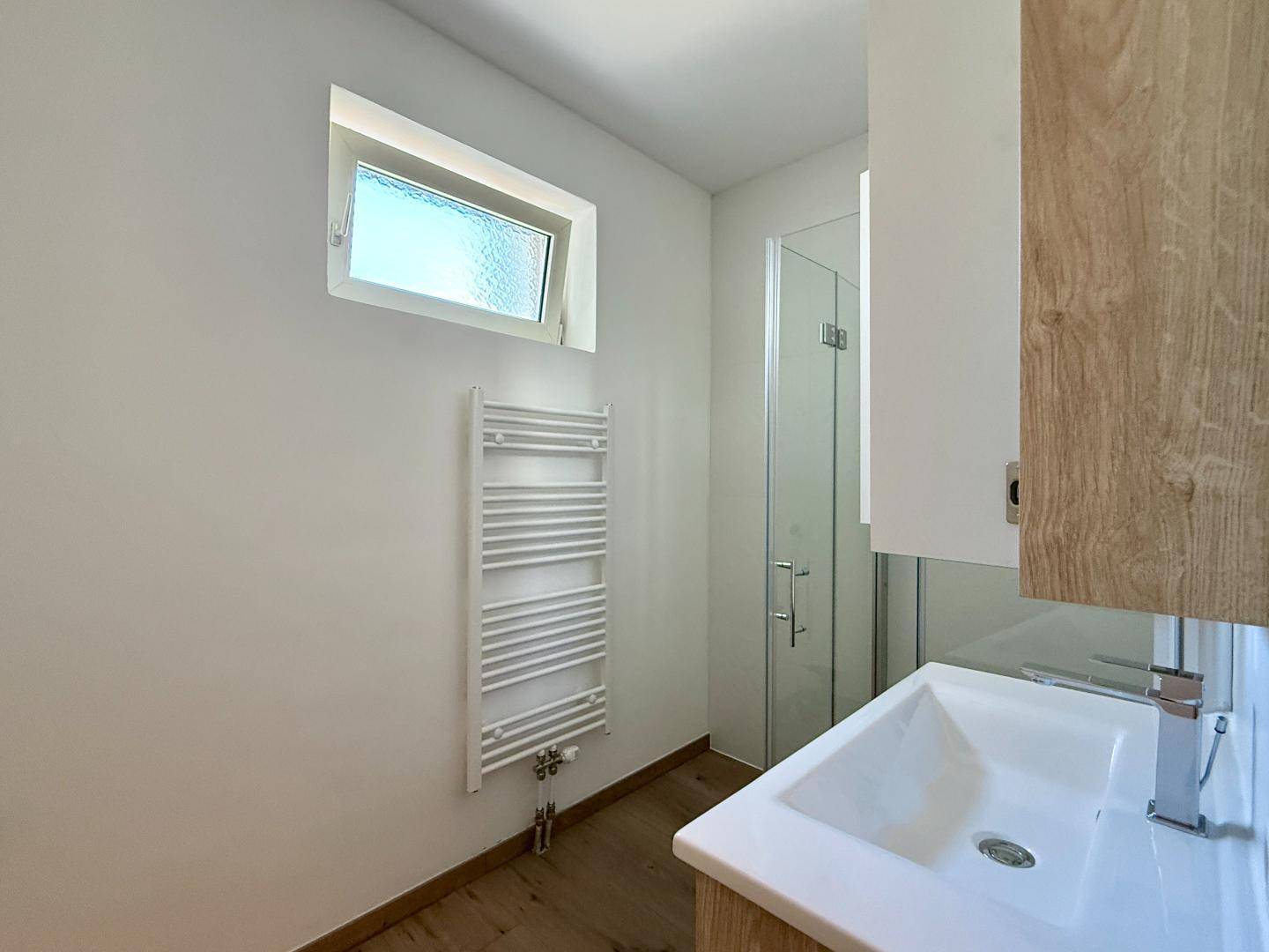 Modernes Badezimmer mit Waschbecken, Spiegelschrank, Dusche und beheiztem Handtuchhalter.