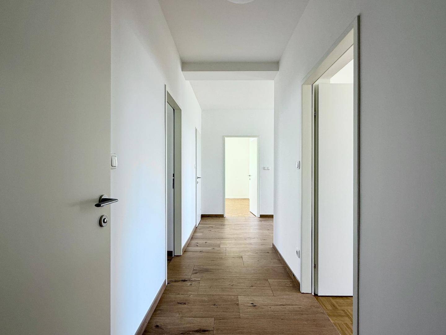 Geräumiger Flur mit Holzboden und Blick auf weitere Zimmer im hinteren Bereich.