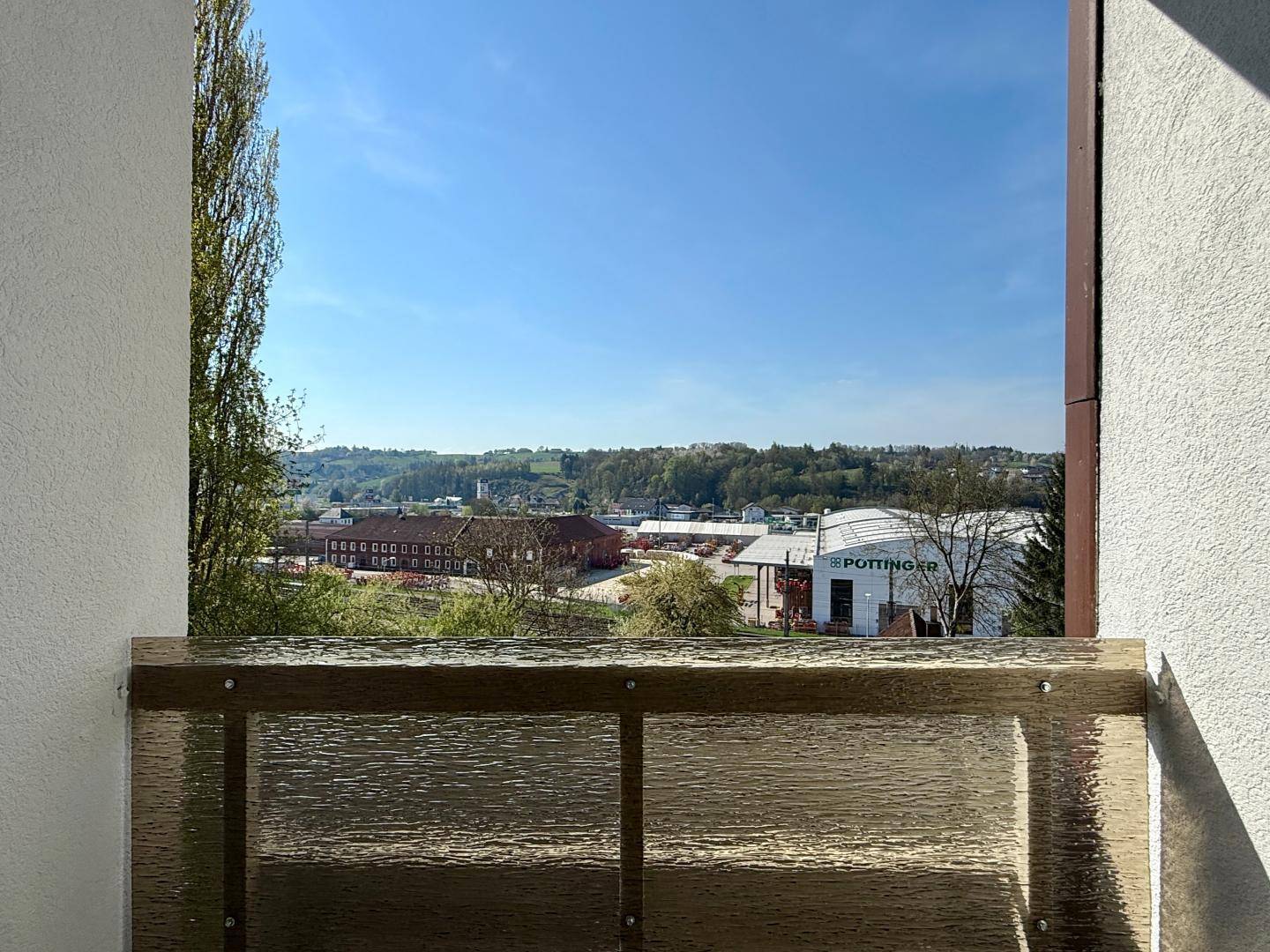 Blick von einem Balkon auf eine grüne Umgebung mit Bäumen und entfernten Gebäuden.