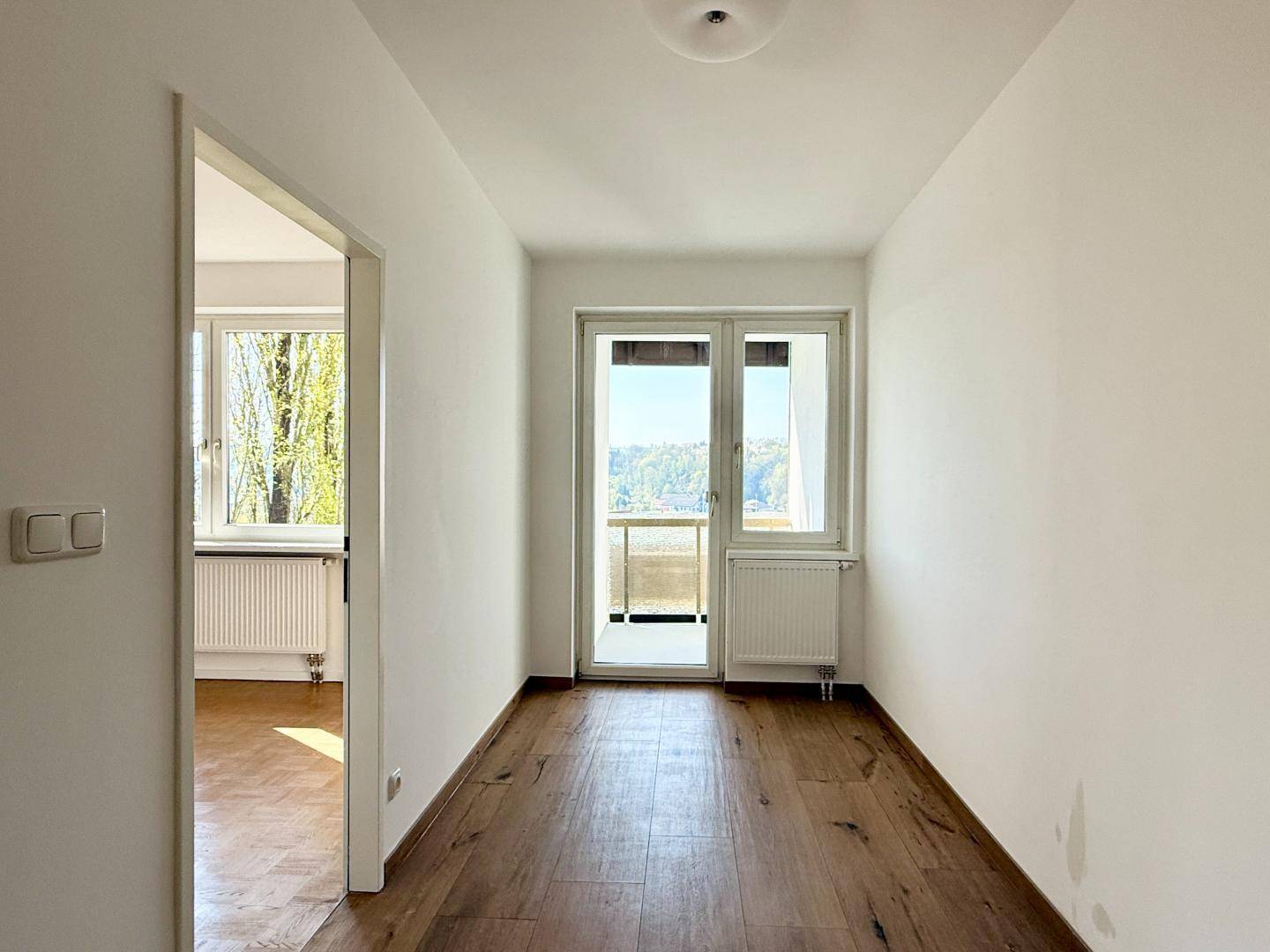 Heller Flur mit Holzboden und Zugang zu einem Balkon mit Weitblick.