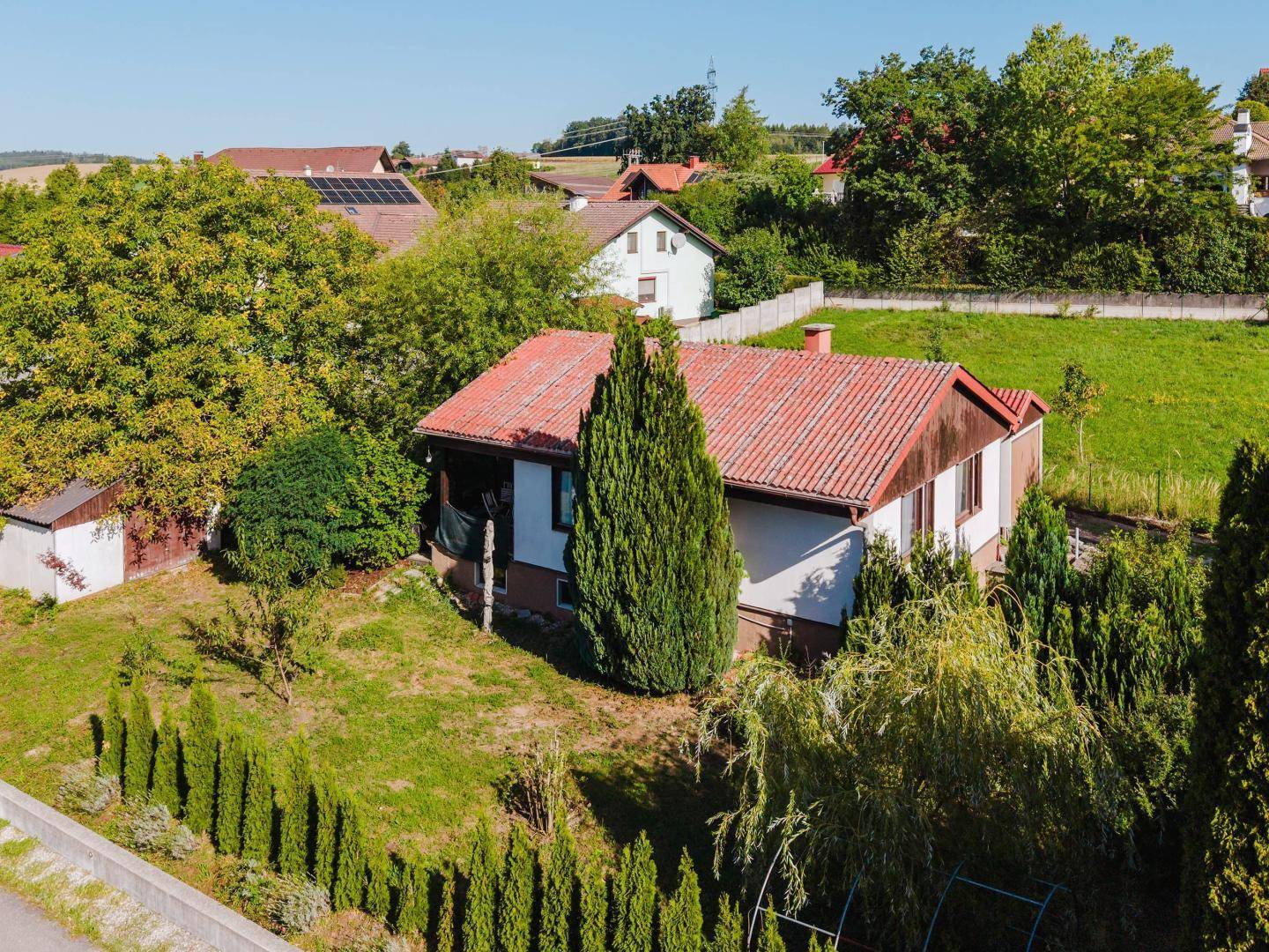 Luftaufnahme des Hauses mit rotem Dach, umgeben von einem grünen Garten und hohen Hecken.