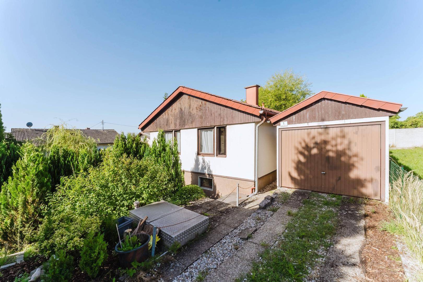 Vorderansicht des Hauses mit integrierter Garage, Zufahrt und umgebenden Büschen.