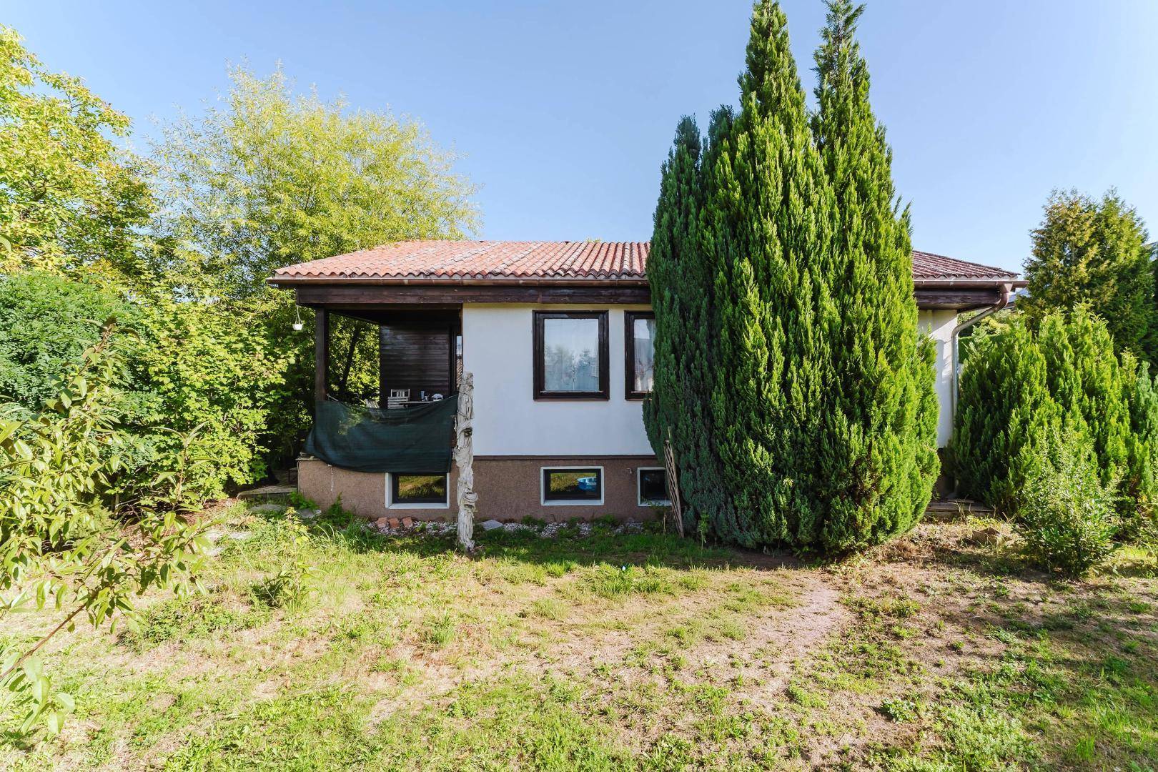 Rückseite des Hauses mit Garten, Bäumen und einer überdachten Terrasse im Erdgeschoss.