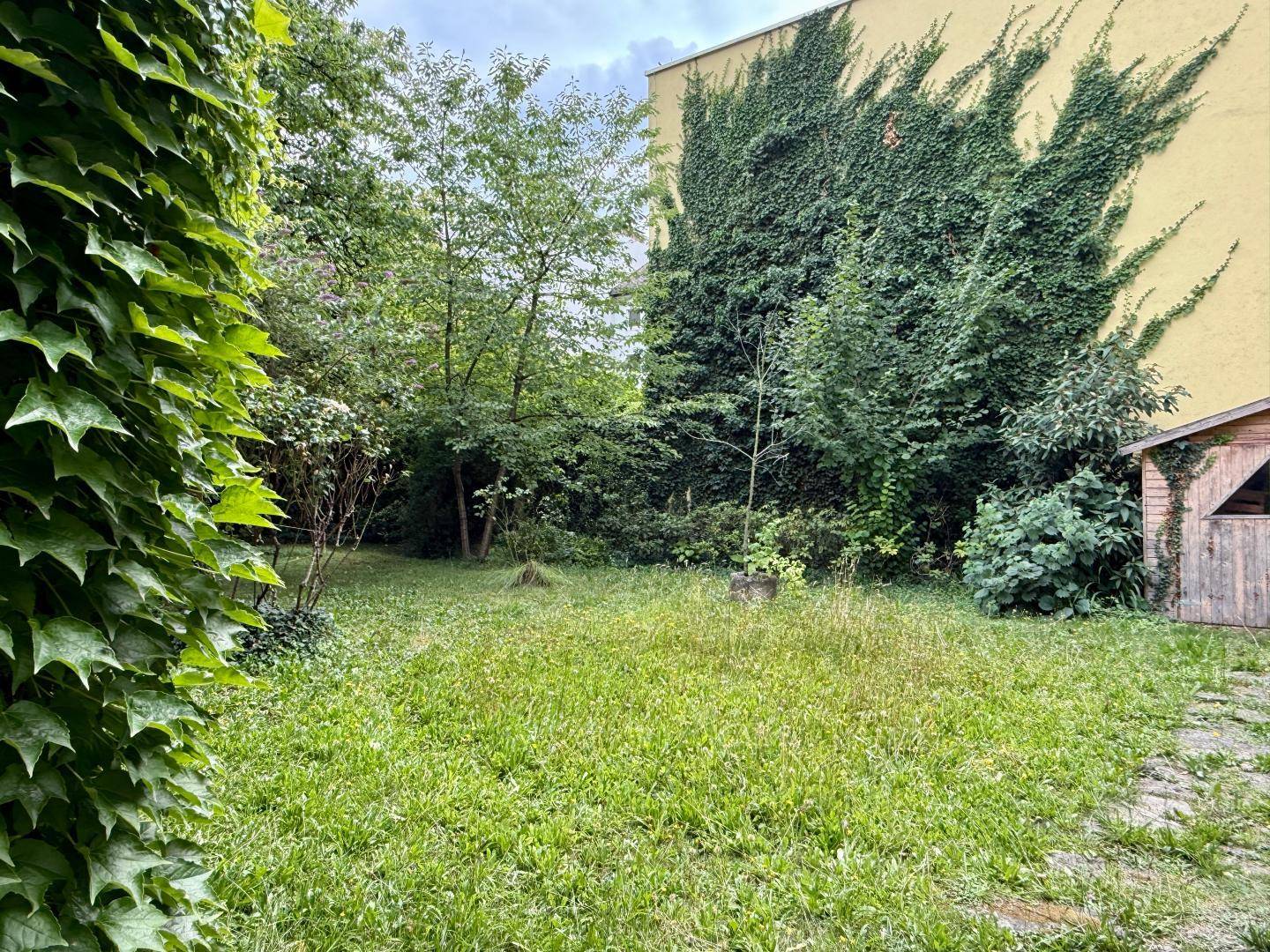 Weitläufiger Garten mit Rasenfläche, Bäumen und einem Gebäude, dessen Fassade mit Efeu bewachsen ist.