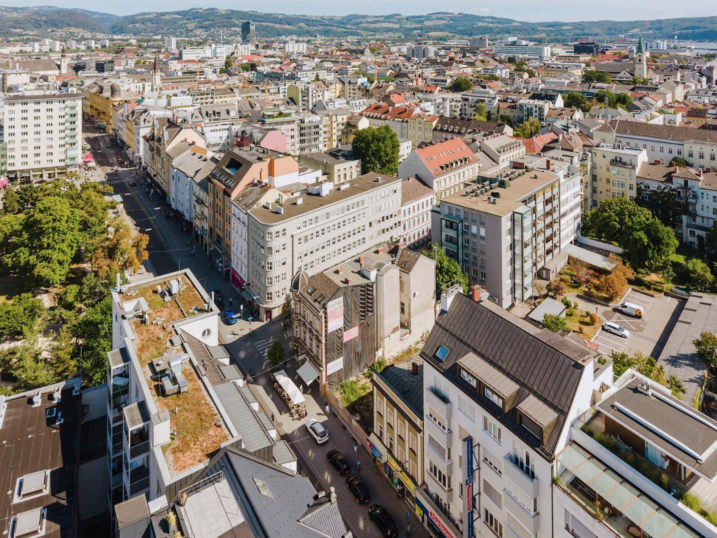 Luftaufnahme einer städtischen Umgebung mit dicht bebauten Straßen, verschiedenen Gebäudetypen und Grünflächen.
