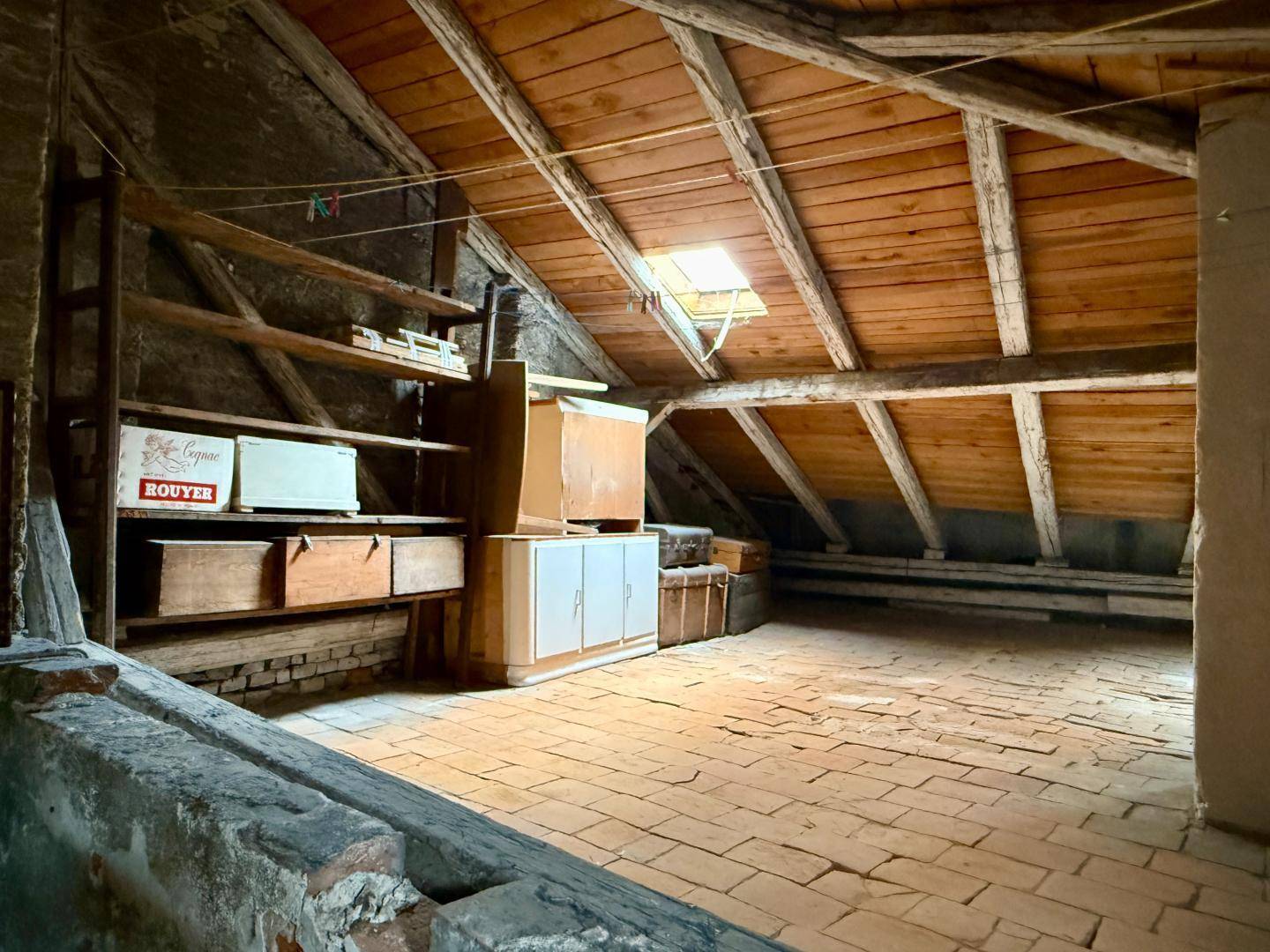 Geräumiger Dachboden mit sichtbaren Holzbalken, Ziegelboden und einem Dachfenster, das Licht spendet.