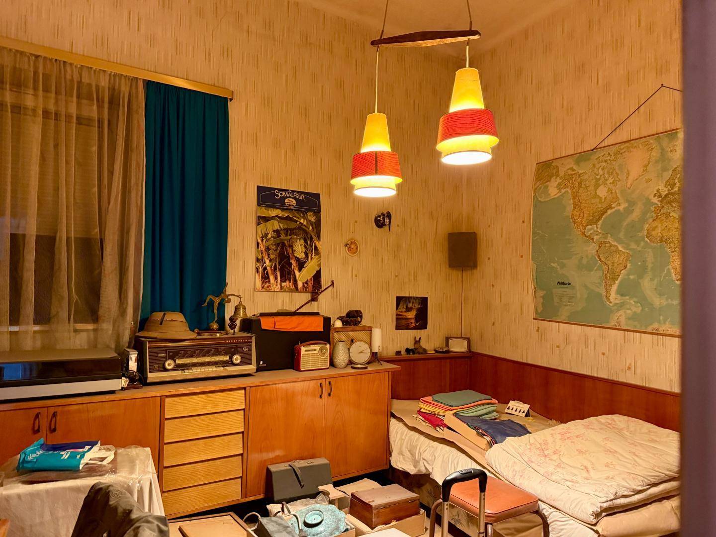 Gemütliches Schlafzimmer im Vintage-Stil mit Tapeten, Holzmöbeln und einem Bett, beleuchtet von Hängelampen.