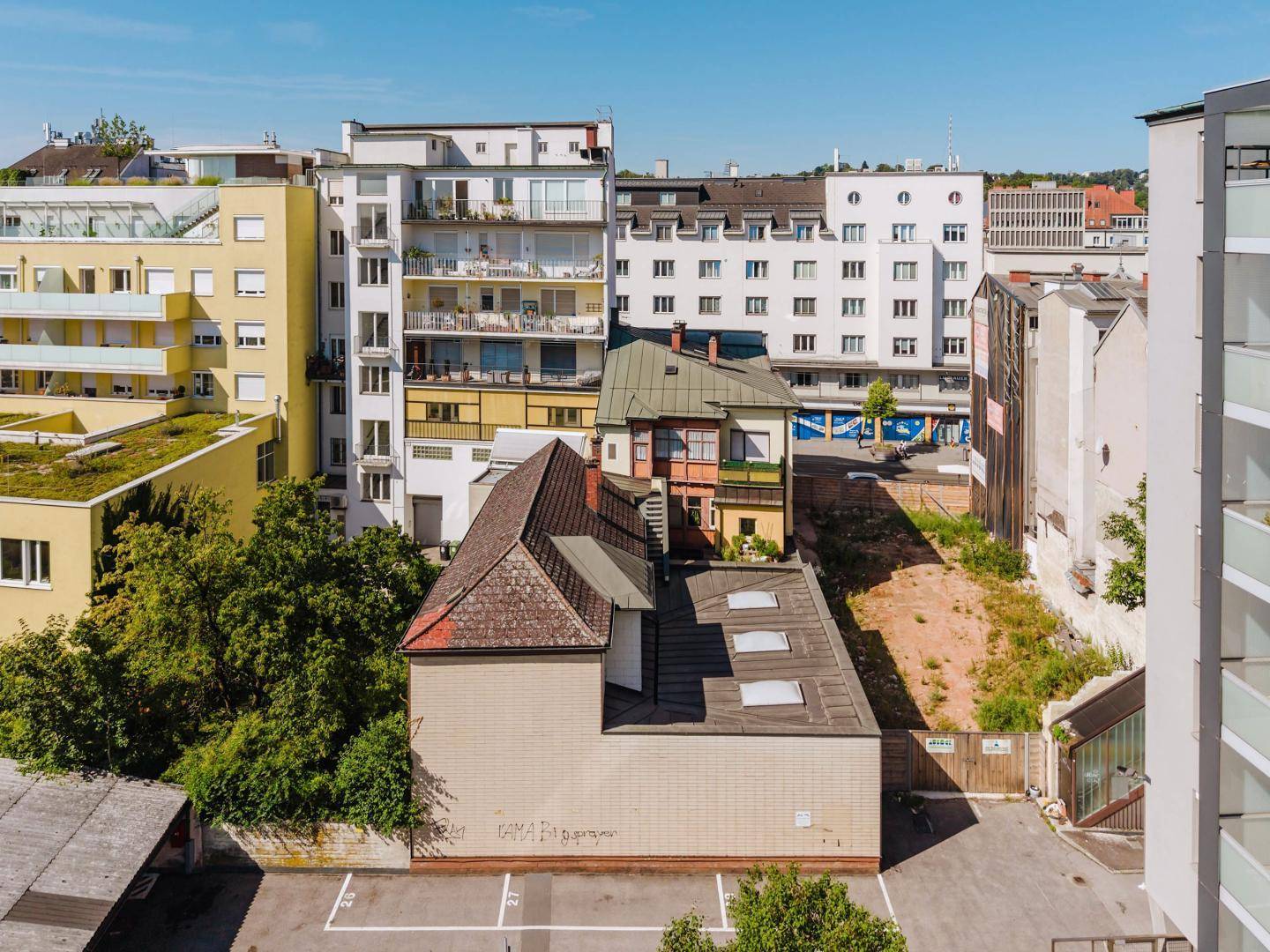 Luftaufnahme eines Gebäudes mit markantem Dach, umgeben von städtischer Bebauung und Parkflächen.