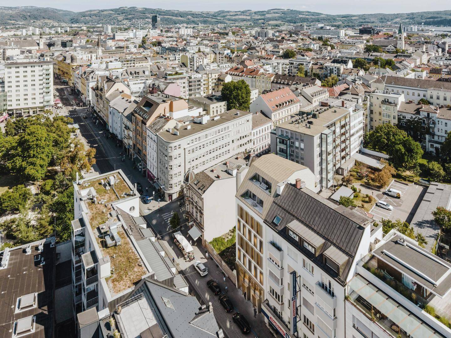 Luftaufnahme einer städtischen Umgebung mit dicht bebauten Straßen, verschiedenen Gebäudetypen und Grünflächen.