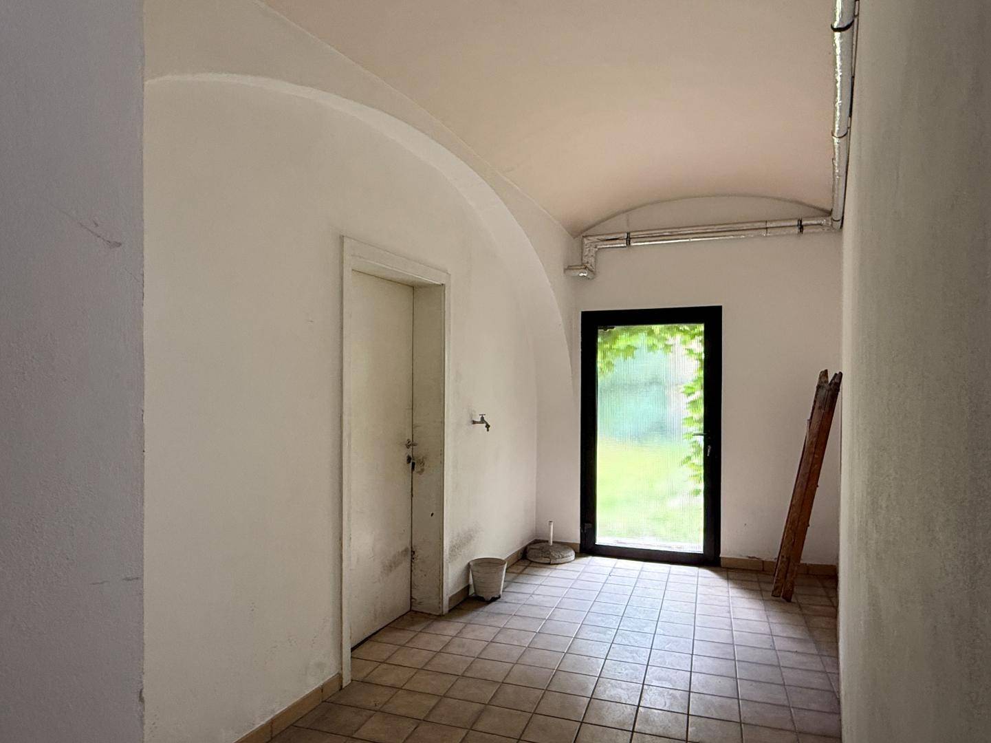 Einfacher Raum mit Fliesenboden, gewölbter Decke und einer Glastür, die ins Freie führt.