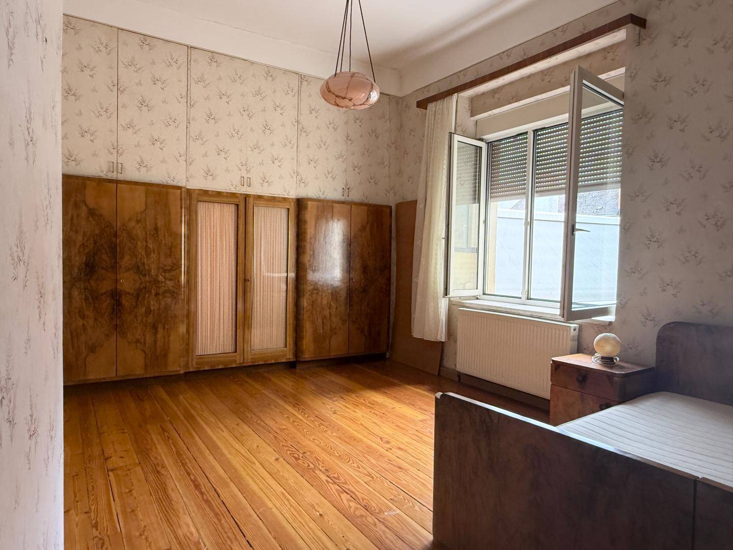Schlafzimmer mit Holzeinbauschränken, Parkettboden und einem Fenster, das Tageslicht hereinlässt.